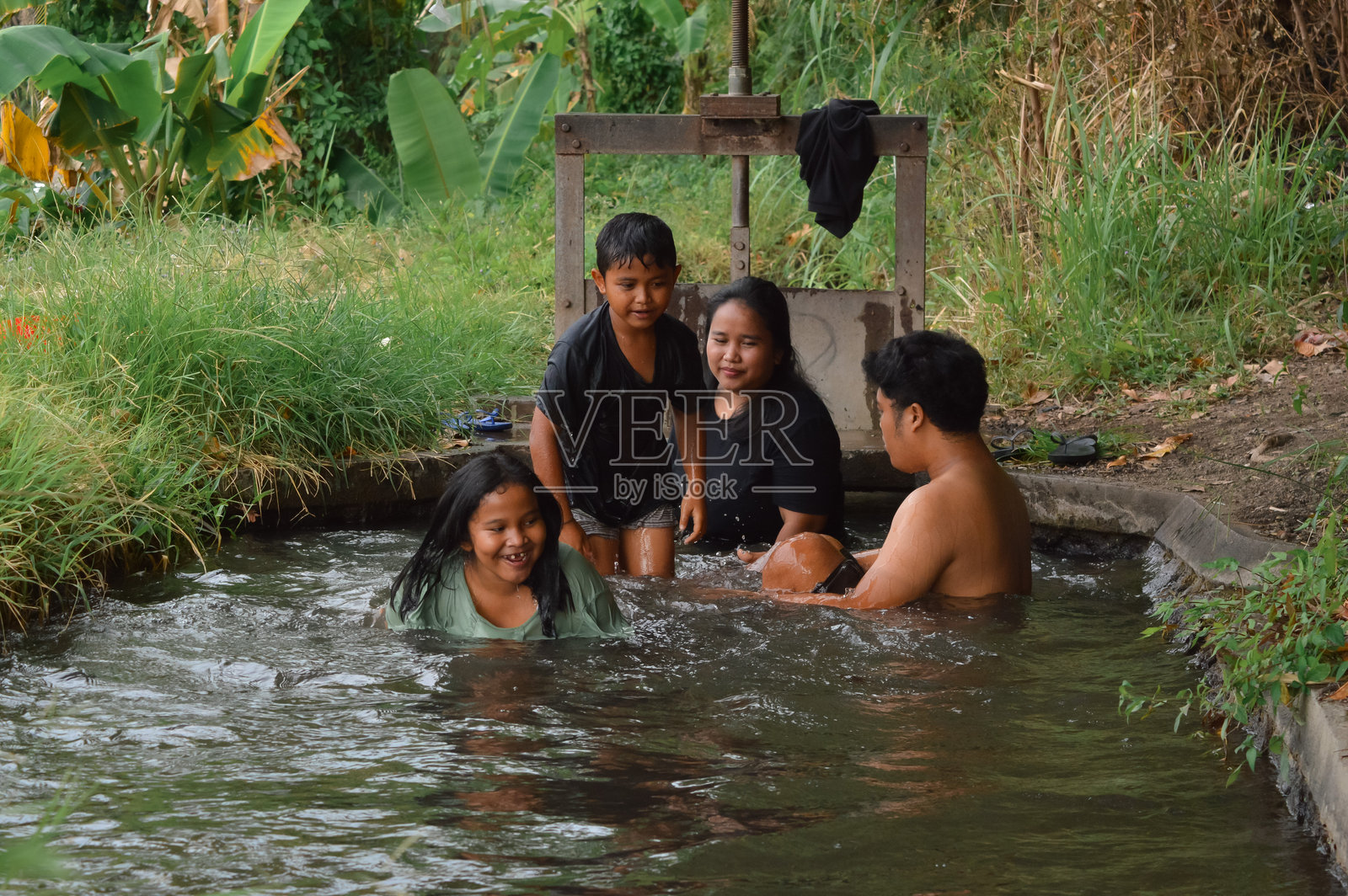 孩子们兴奋地在灌溉渠中洗澡，父母在旁边陪伴。照片摄影图片