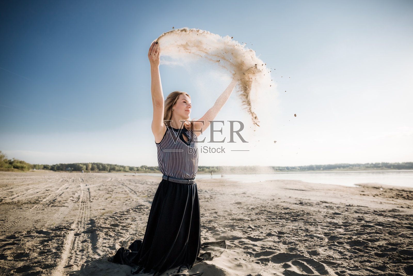 一位年轻美丽的欧洲女孩在黄昏日落时分，站在大自然中，手中撒着沙子，迎着风。这是一场人与自然共舞的仪式。照片摄影图片