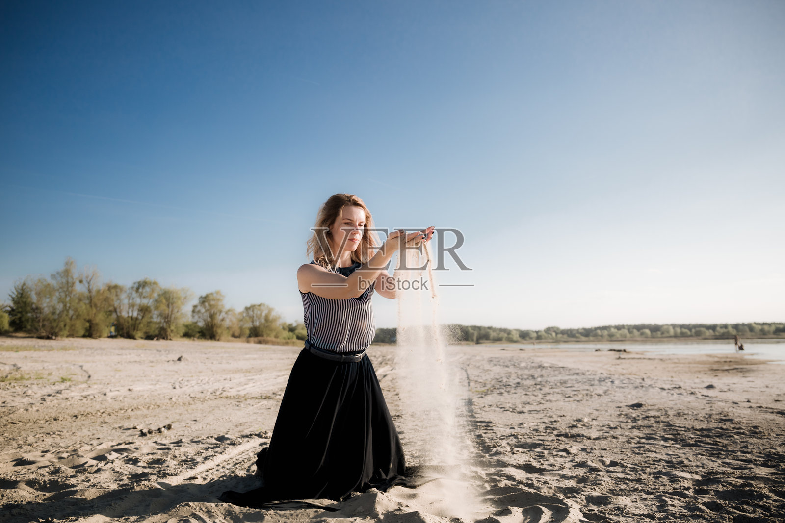 一个年轻美丽的欧洲女孩在黄昏日落时分，站在大自然中，手中撒着沙子，迎着风。这是一场人与自然共舞的仪式。照片摄影图片