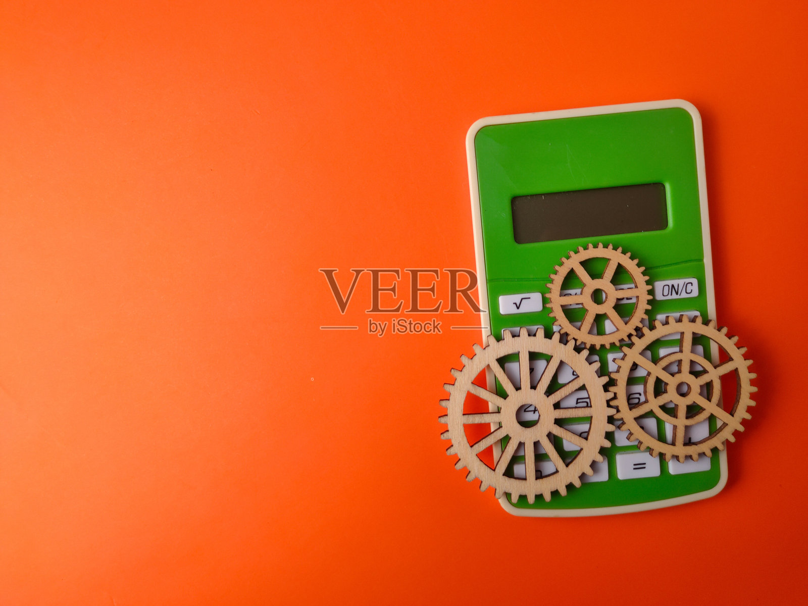 图像展示了一台绿色计算器，旁边有三个木质齿轮，背景为橙色。照片摄影图片