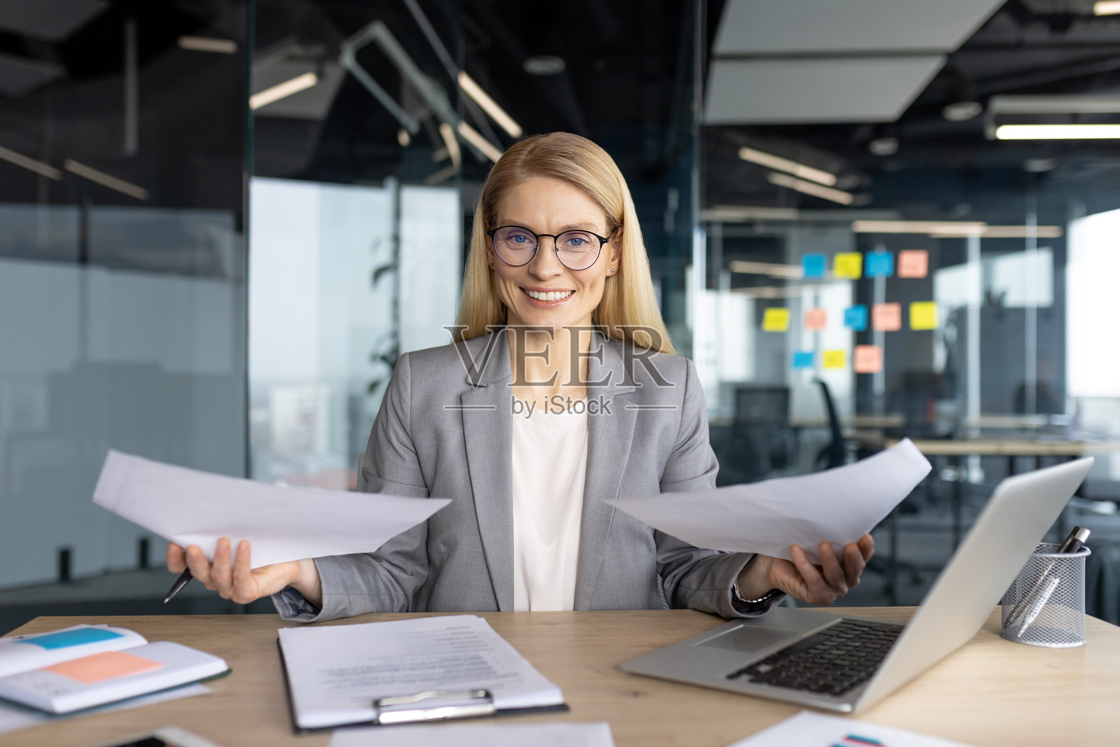 在现代办公室环境中，热情工作的女商人，手边有文件和笔记本电脑。照片摄影图片