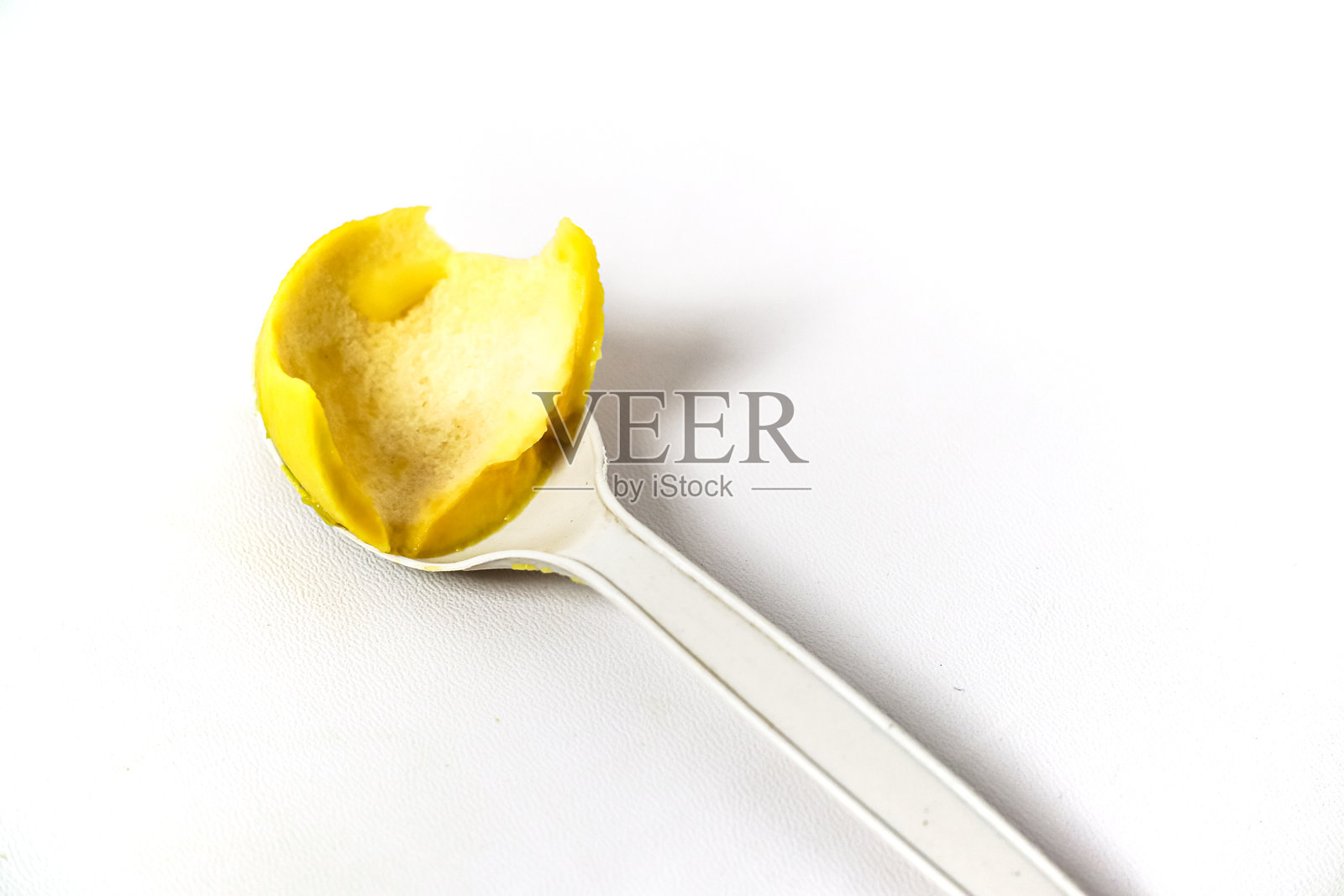 白色背景下，一勺黄色果肉特写，咬了一口。照片摄影图片