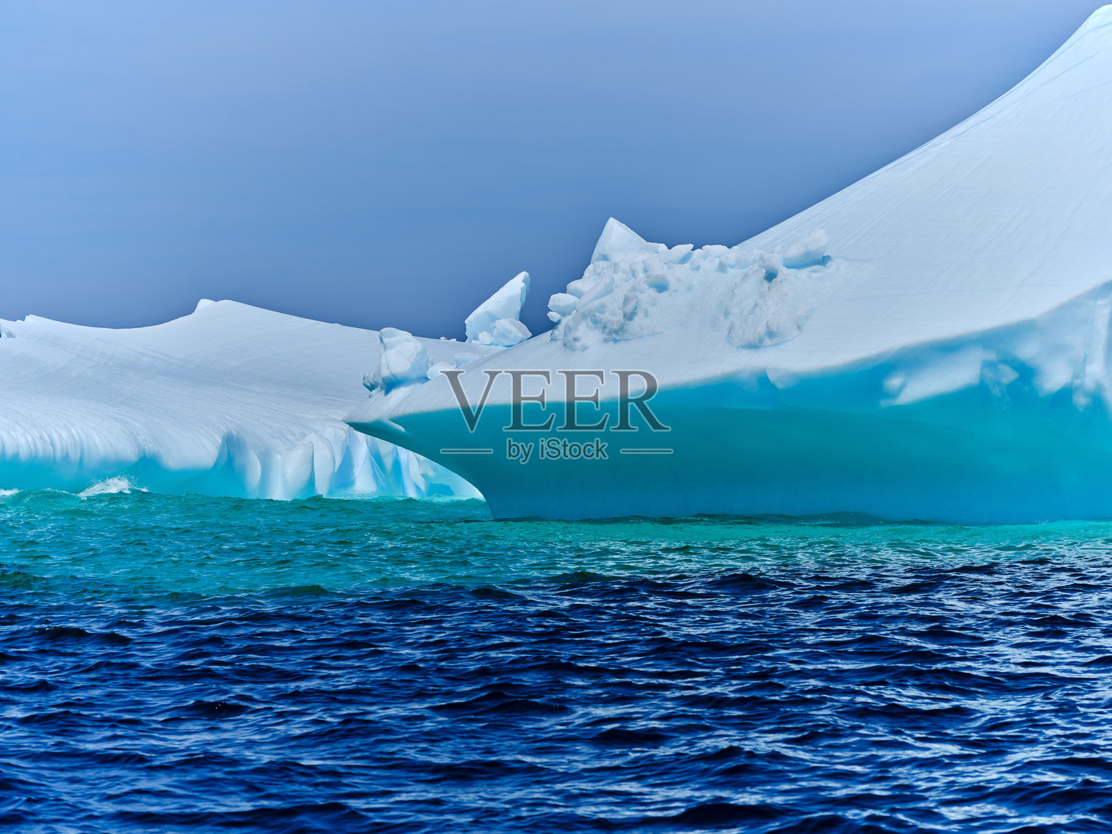 绿色的水显示了冰山在水下延伸的距离。照片摄影图片