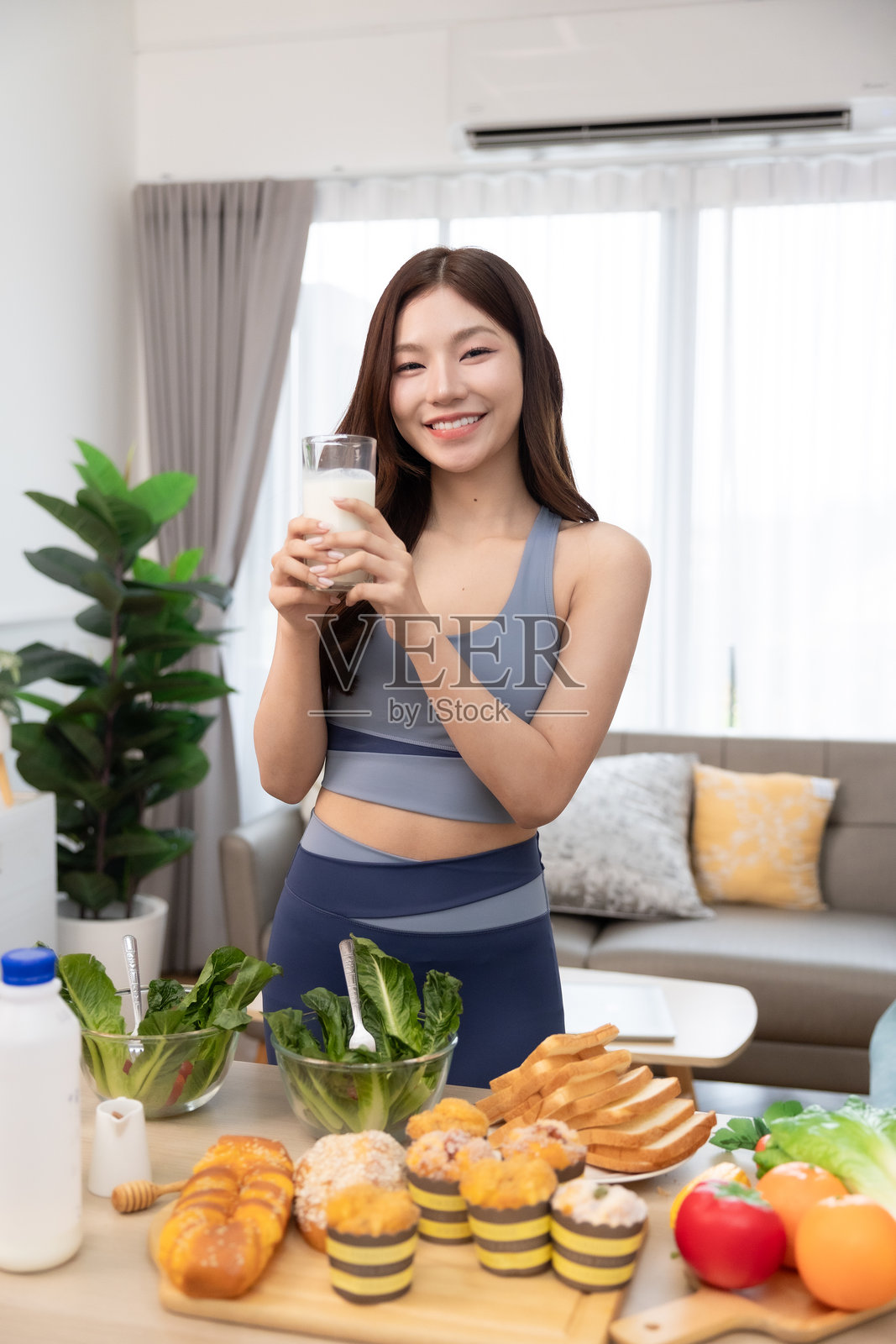 年轻的亚洲运动女性在家准备蛋白质奶昔。饮食与健康食品。训练后放松。美丽的年轻女性在锻炼后喝牛奶。健康生活方式的概念。照片摄影图片