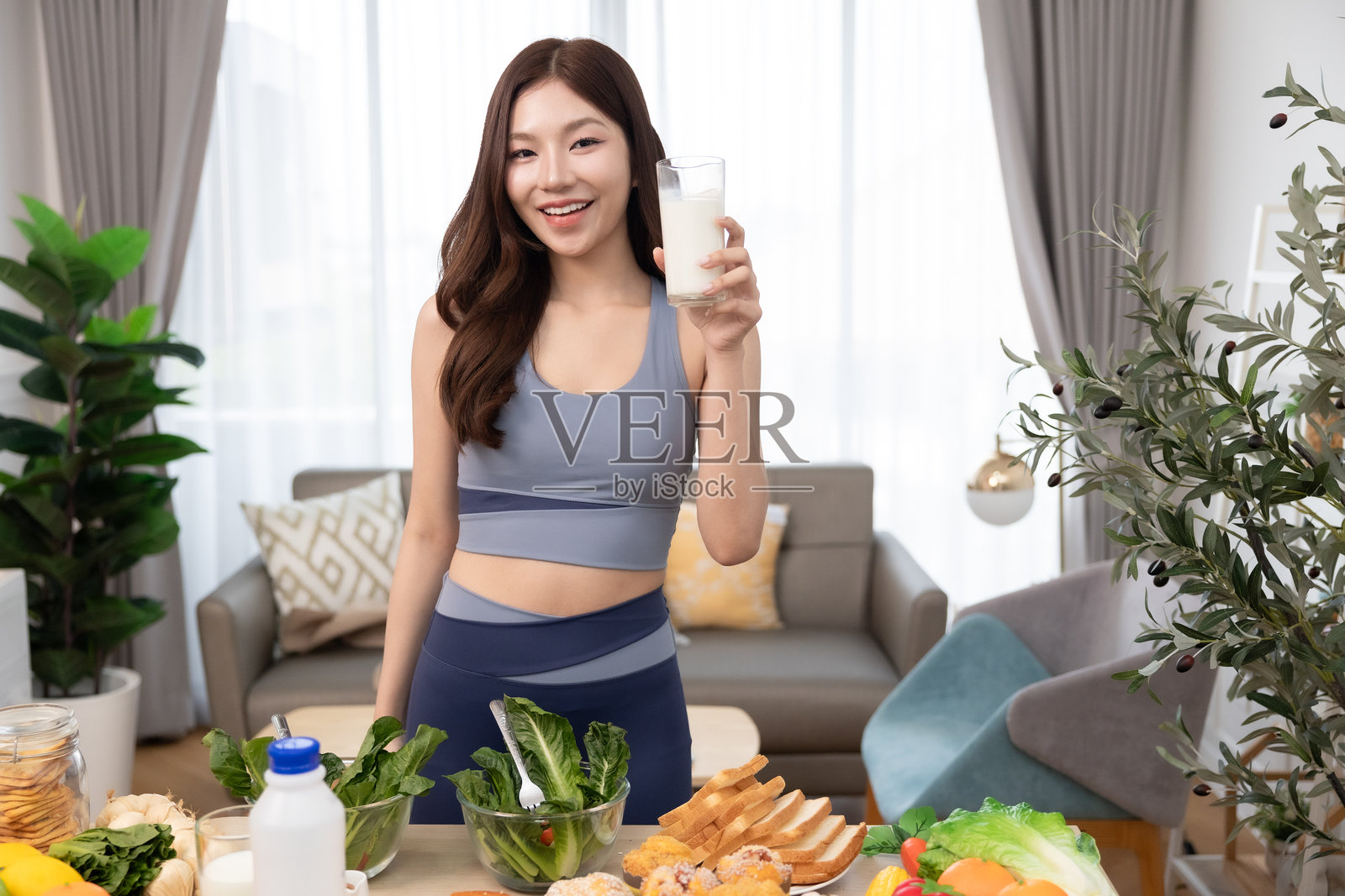 年轻的亚洲运动女性在家准备蛋白质奶昔。饮食与健康食品。训练后放松。美丽的年轻女性在锻炼后喝牛奶。健康生活方式的概念。照片摄影图片