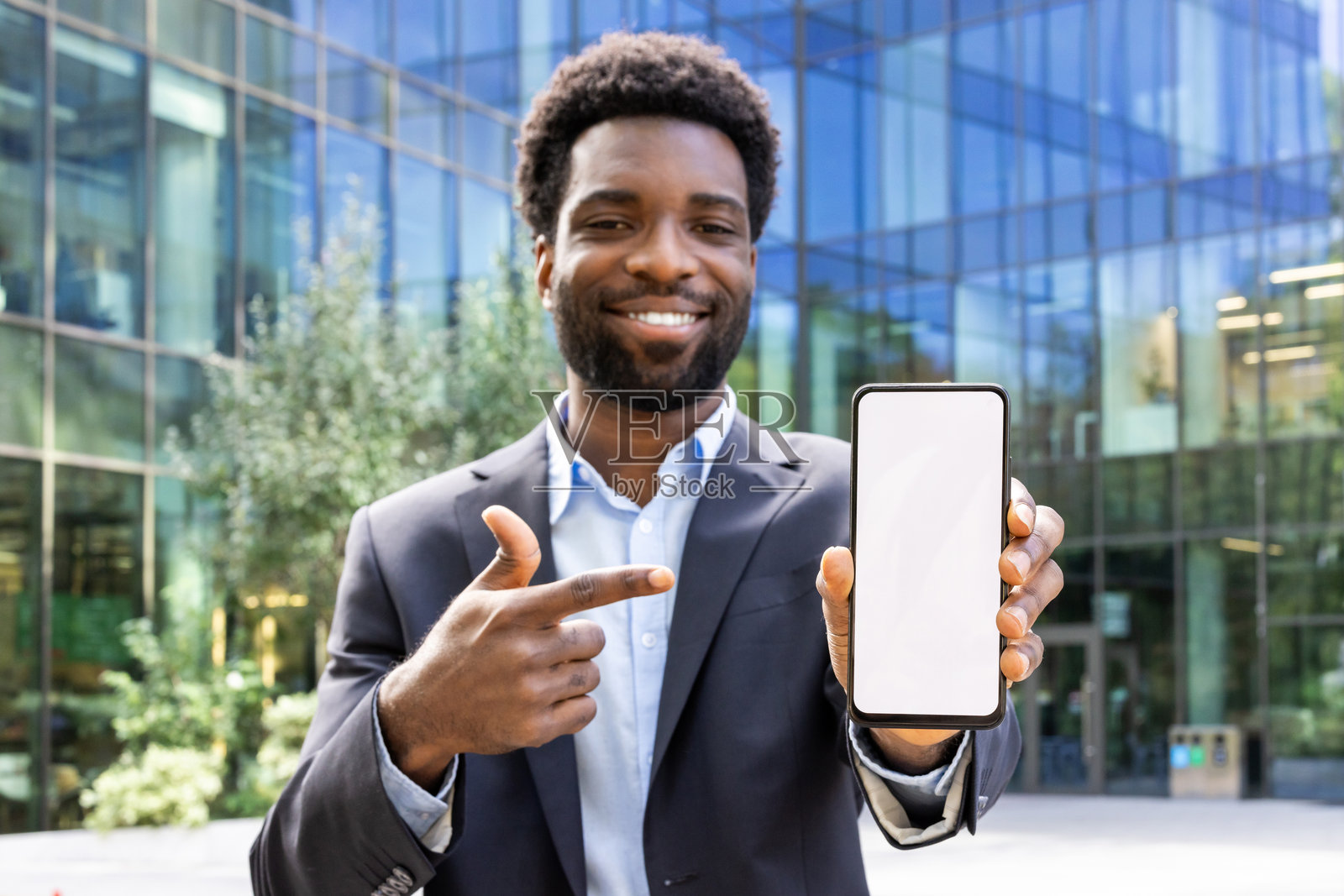 快乐的商人穿着西装，展示一部空白屏幕的智能手机。照片摄影图片