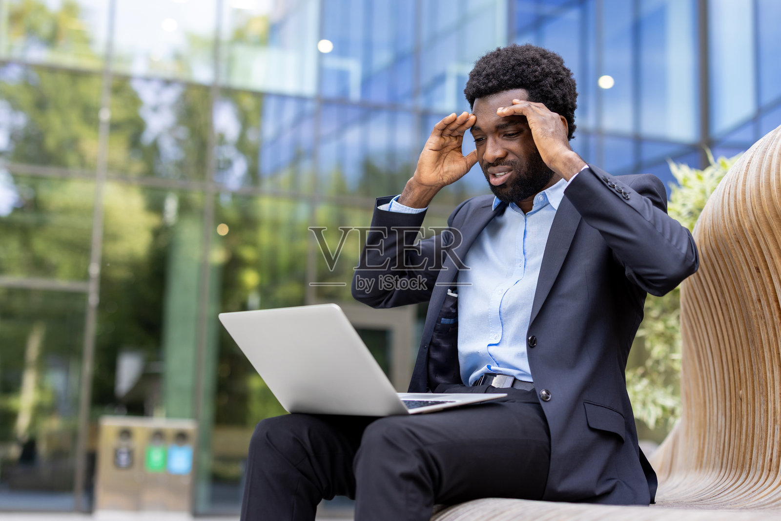 一位感到压力的商人在户外使用笔记本电脑时头痛。照片摄影图片