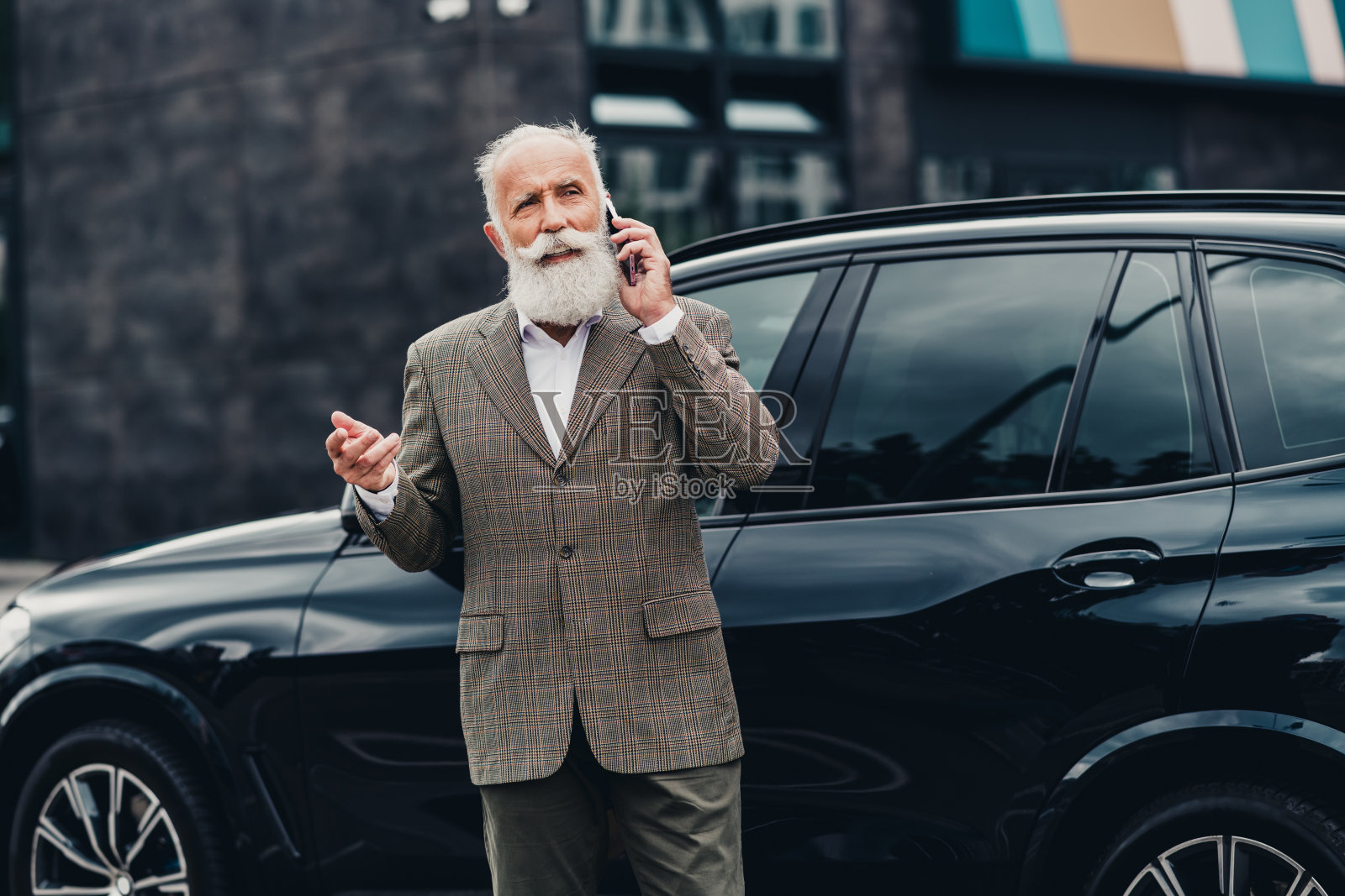 成熟的商人在户外靠着汽车打电话，展现出都市优雅和专业风范，穿着时尚的服装。照片摄影图片