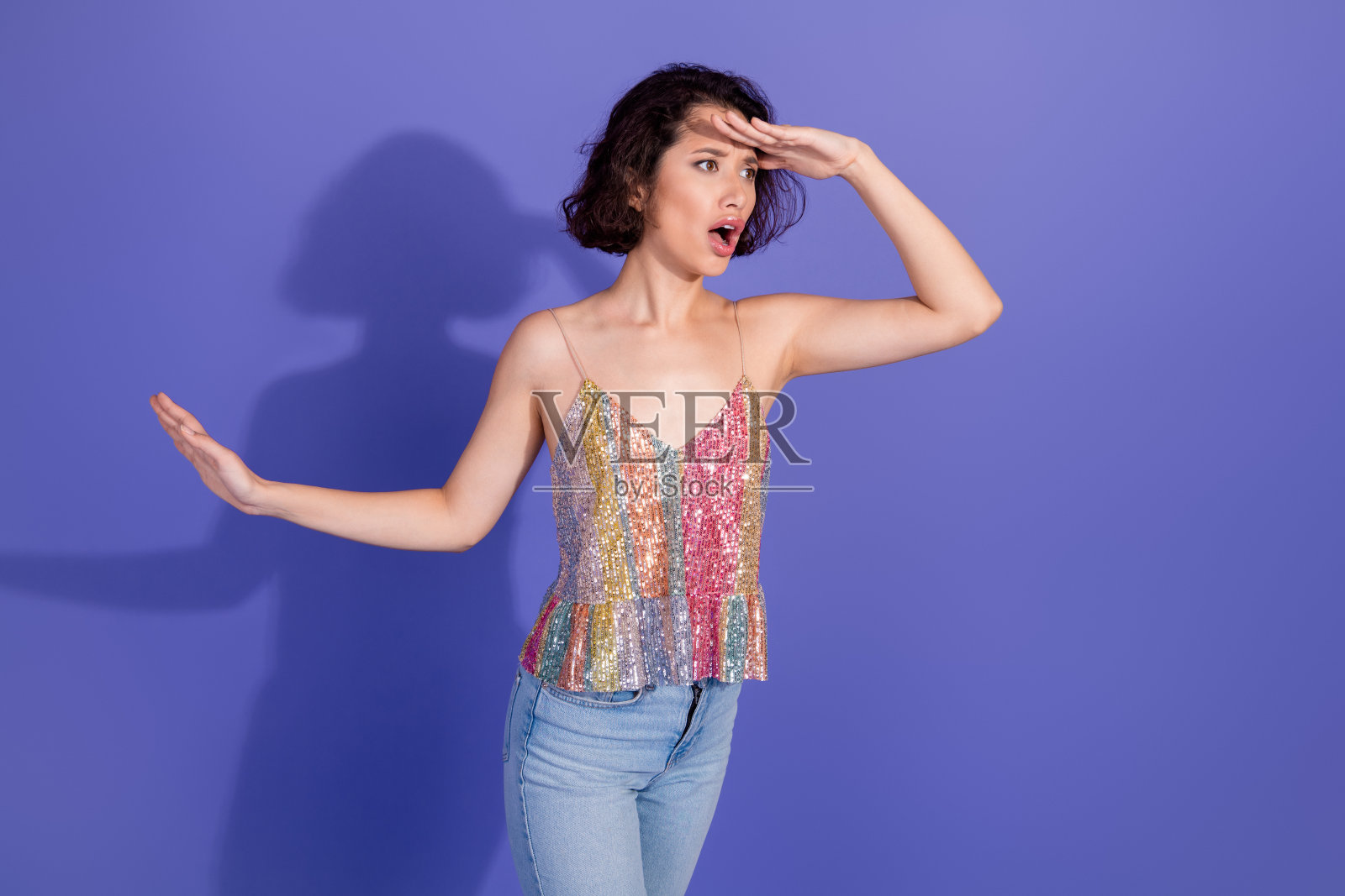 穿着闪亮服装的快乐时尚女性在紫色背景前创意摆姿，展现出好奇和魅力。照片摄影图片