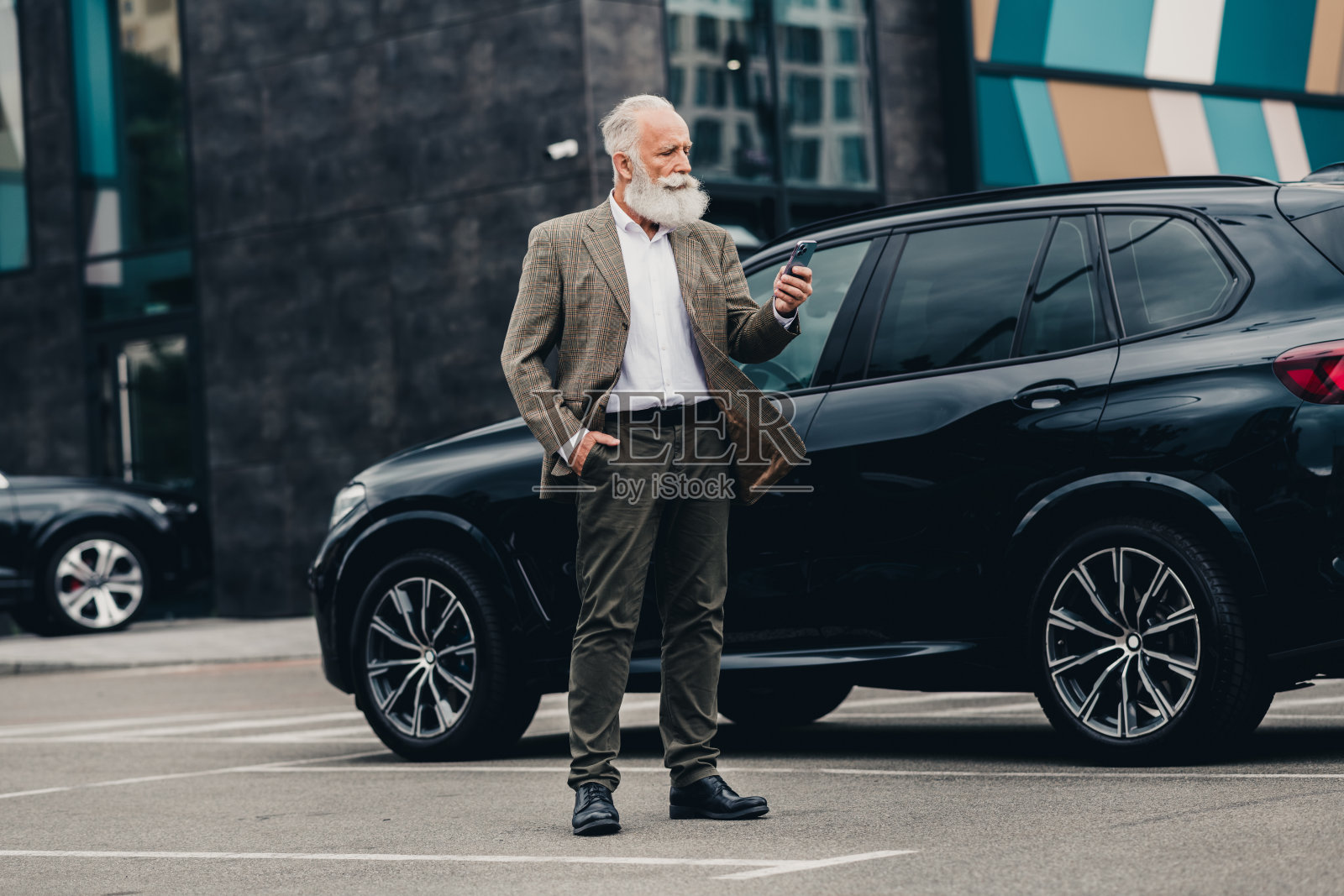 成熟的职业商人在城市户外环境中自信地站在他的车旁，使用智能手机。照片摄影图片