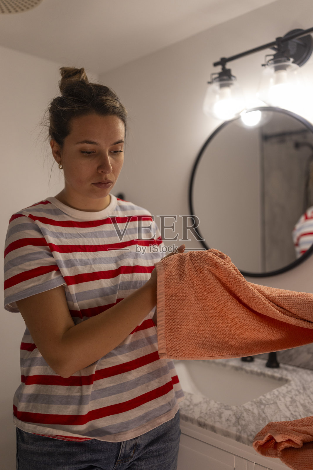 年轻女性在浴室里折叠明亮的橙色毛巾照片摄影图片