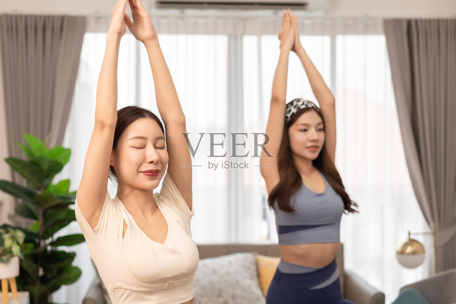 一对情侣，女性在家锻炼。年轻女性在公寓的垫子上做瑜伽，观看教程，使用笔记本电脑。在家训练并观看数字平板上的在线课程。照片摄影图片