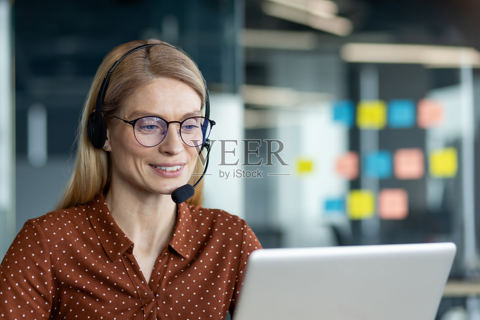 在办公室里，专业女性佩戴耳机，使用笔记本电脑远程工作。照片摄影图片