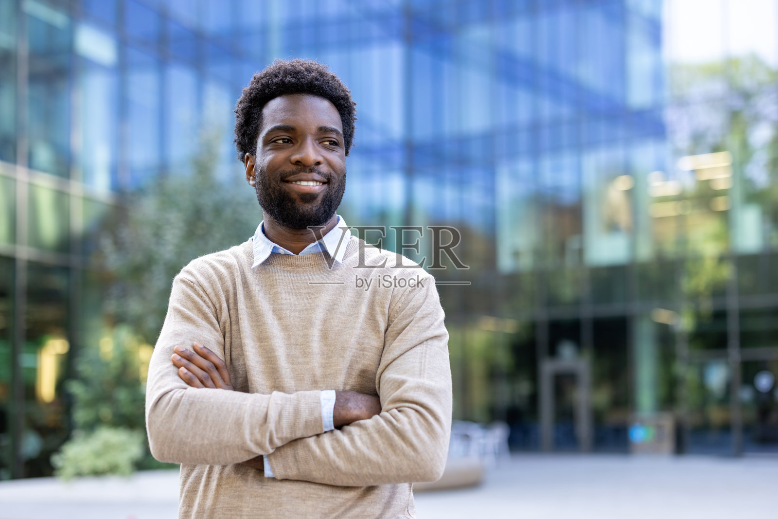 自信的男人在现代办公楼附近站立，双臂交叉。照片摄影图片
