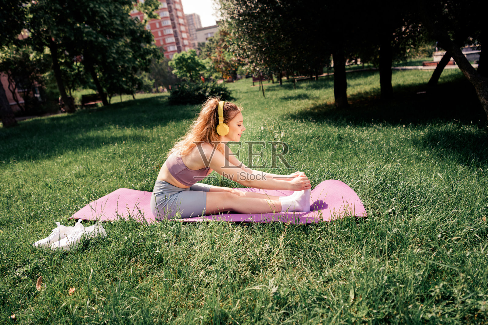 年轻女性在夏季公园户外练习瑜伽，戴着耳机，享受阳光明媚的锻炼时光。照片摄影图片