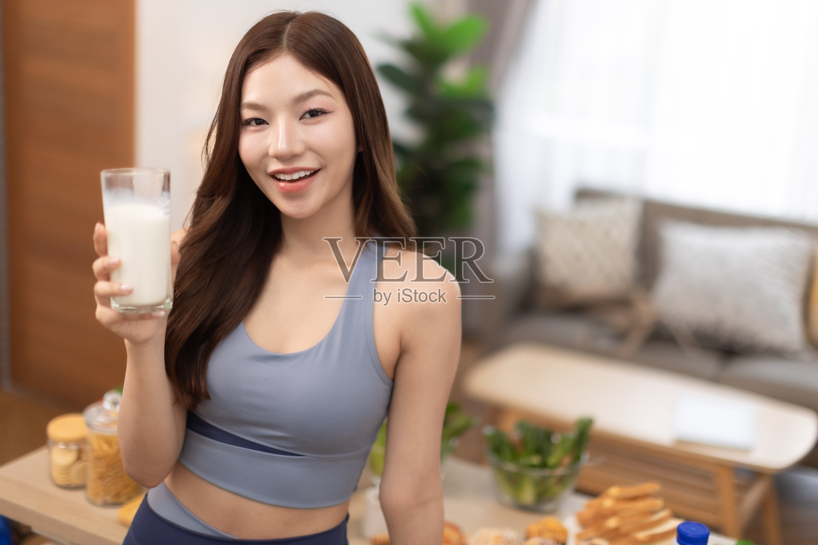 年轻的亚洲运动女性在家准备蛋白质奶昔。饮食与健康食品。训练后放松。美丽的年轻女性在锻炼后喝牛奶。健康生活方式的概念。照片摄影图片