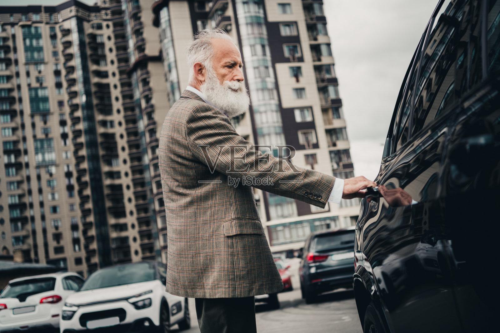身穿正式服装的老年绅士在城市环境中打开车门，展现出风格、自信和专业。照片摄影图片