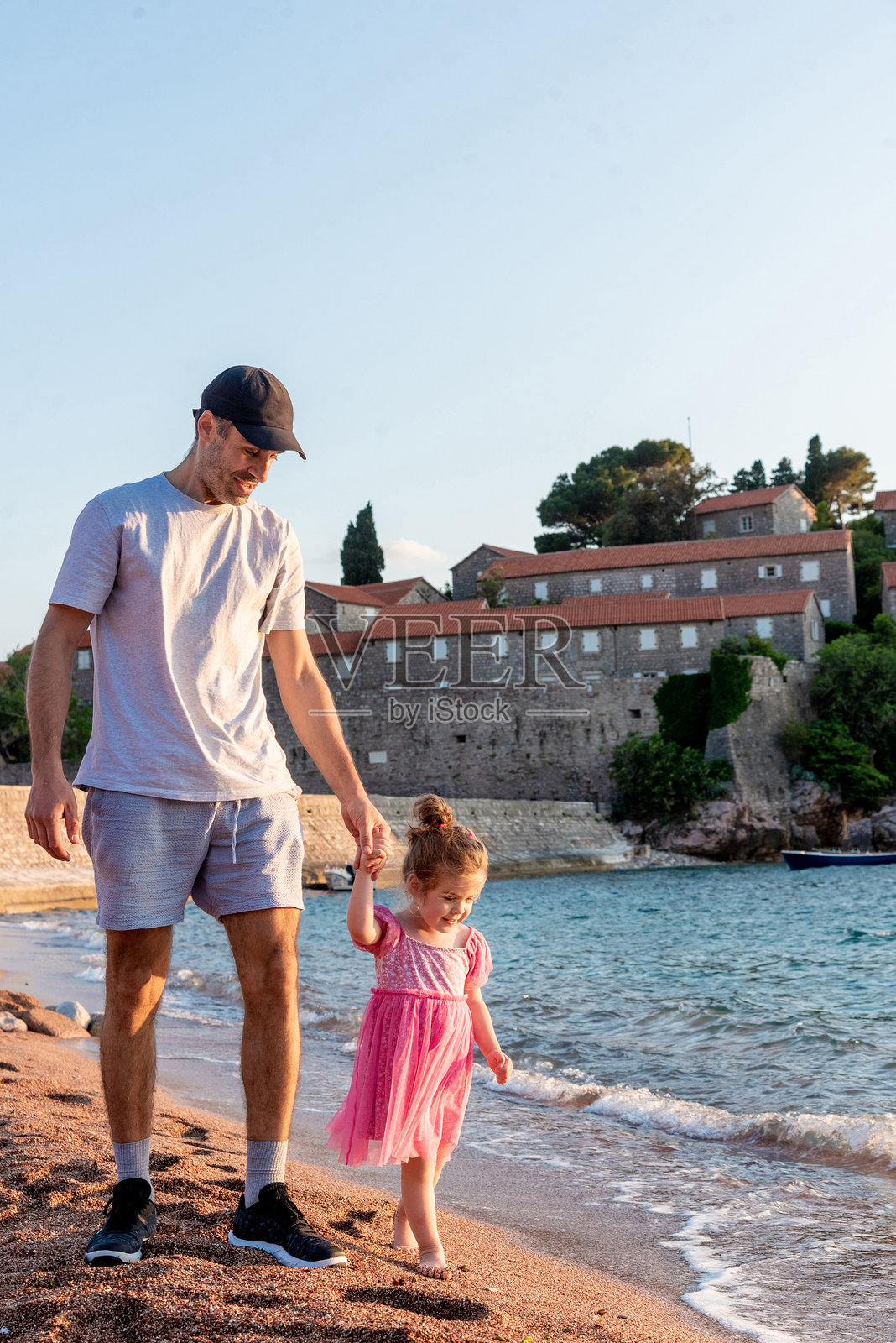 父亲和女儿在海滩上散步，男人和女孩在夏季假期中。照片摄影图片