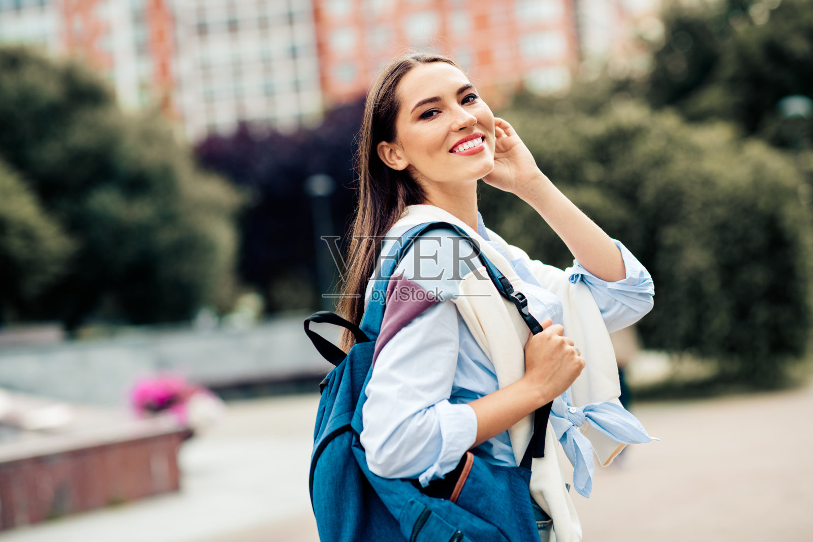 年轻女性在阳光明媚的城市环境中背着背包微笑照片摄影图片