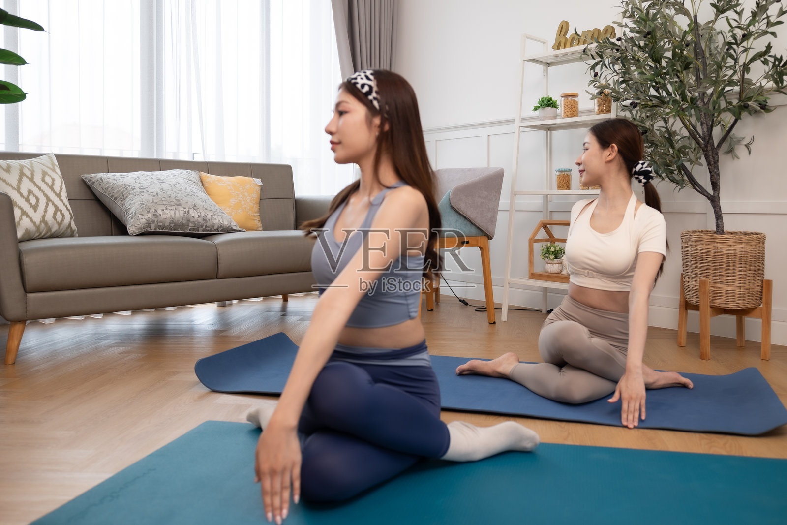 一对情侣，女性在家锻炼。年轻女性在公寓的垫子上做瑜伽，观看教程，使用笔记本电脑。在家训练并观看数字平板上的在线课程。照片摄影图片