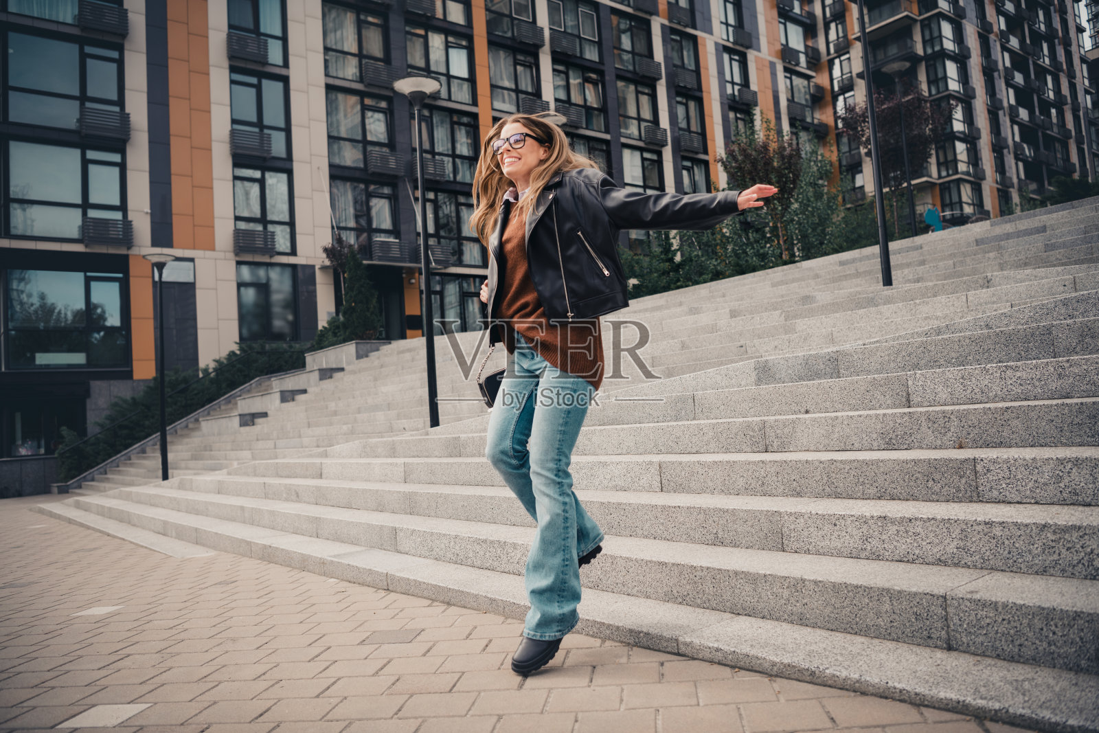 时尚年轻女性在阳光明媚的日子里，穿着休闲服装，悠闲地在现代城市建筑中漫步。照片摄影图片