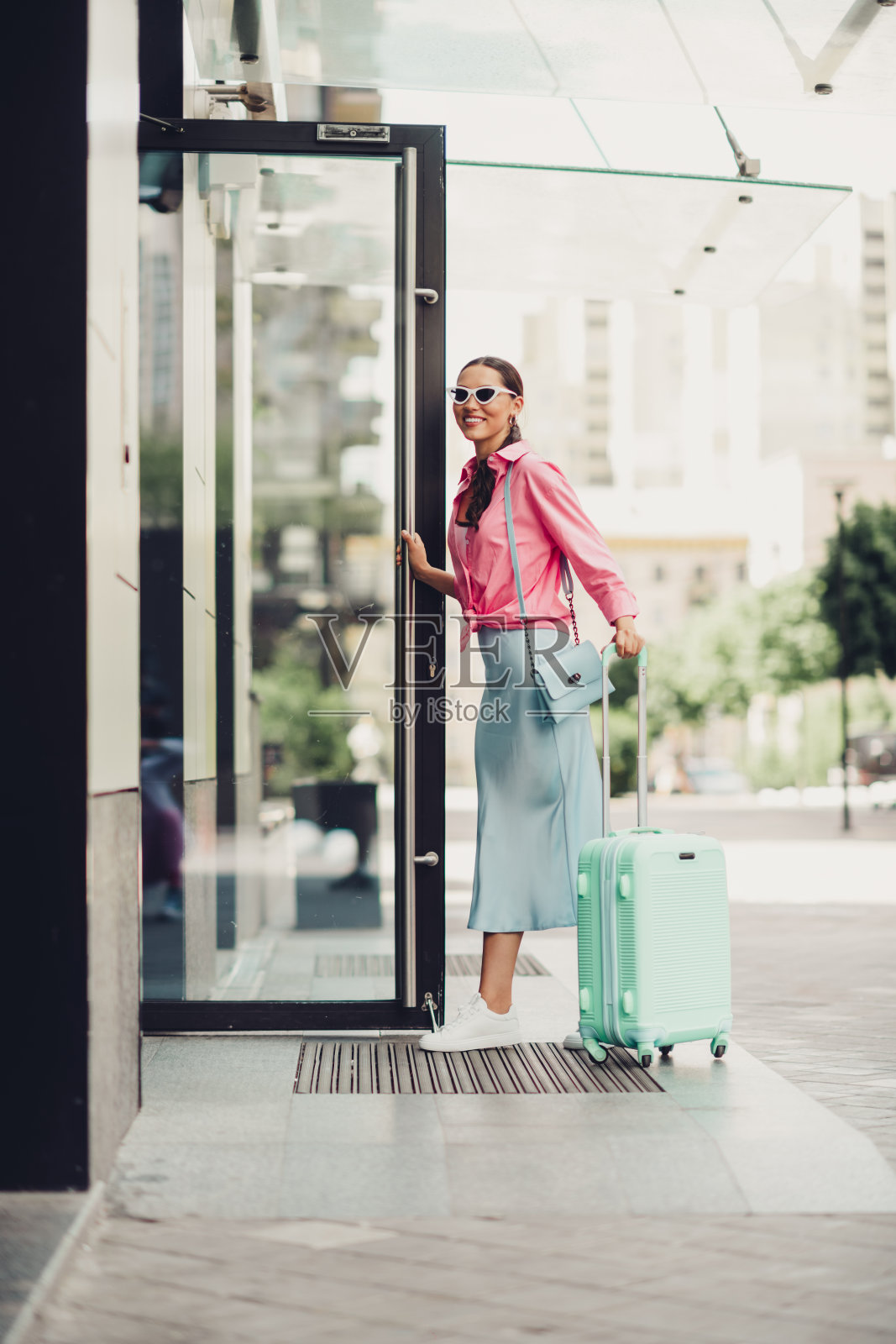 时尚年轻女性带着行李箱在阳光明媚的日子里走进城市建筑照片摄影图片