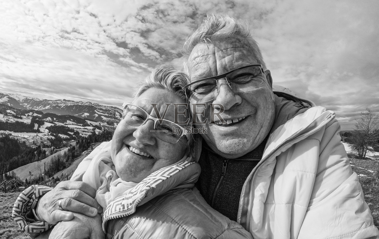 快乐的老年夫妇在冬季徒步旅行的山顶拍自拍 - 爱与快乐的老年生活方式概念 - 重点在面部 - 黑白编辑照片摄影图片