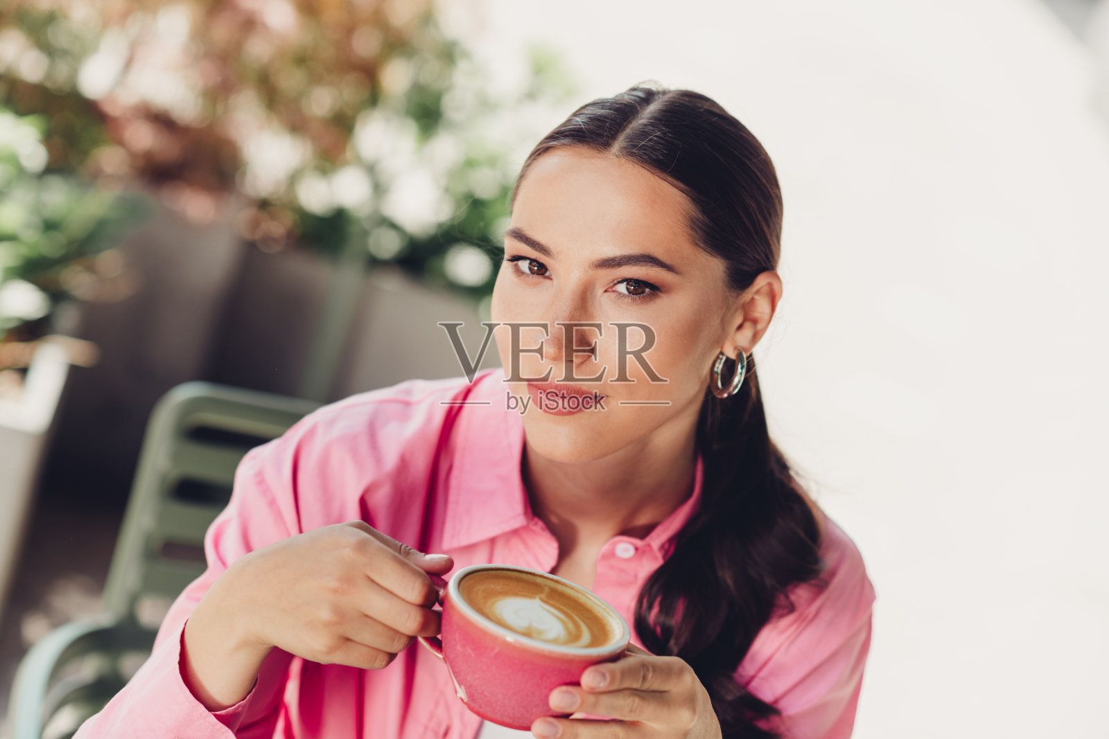 迷人的女性在阳光明媚的日子里户外享受一杯咖啡，穿着休闲的粉色服装，显得时尚而快乐。照片摄影图片