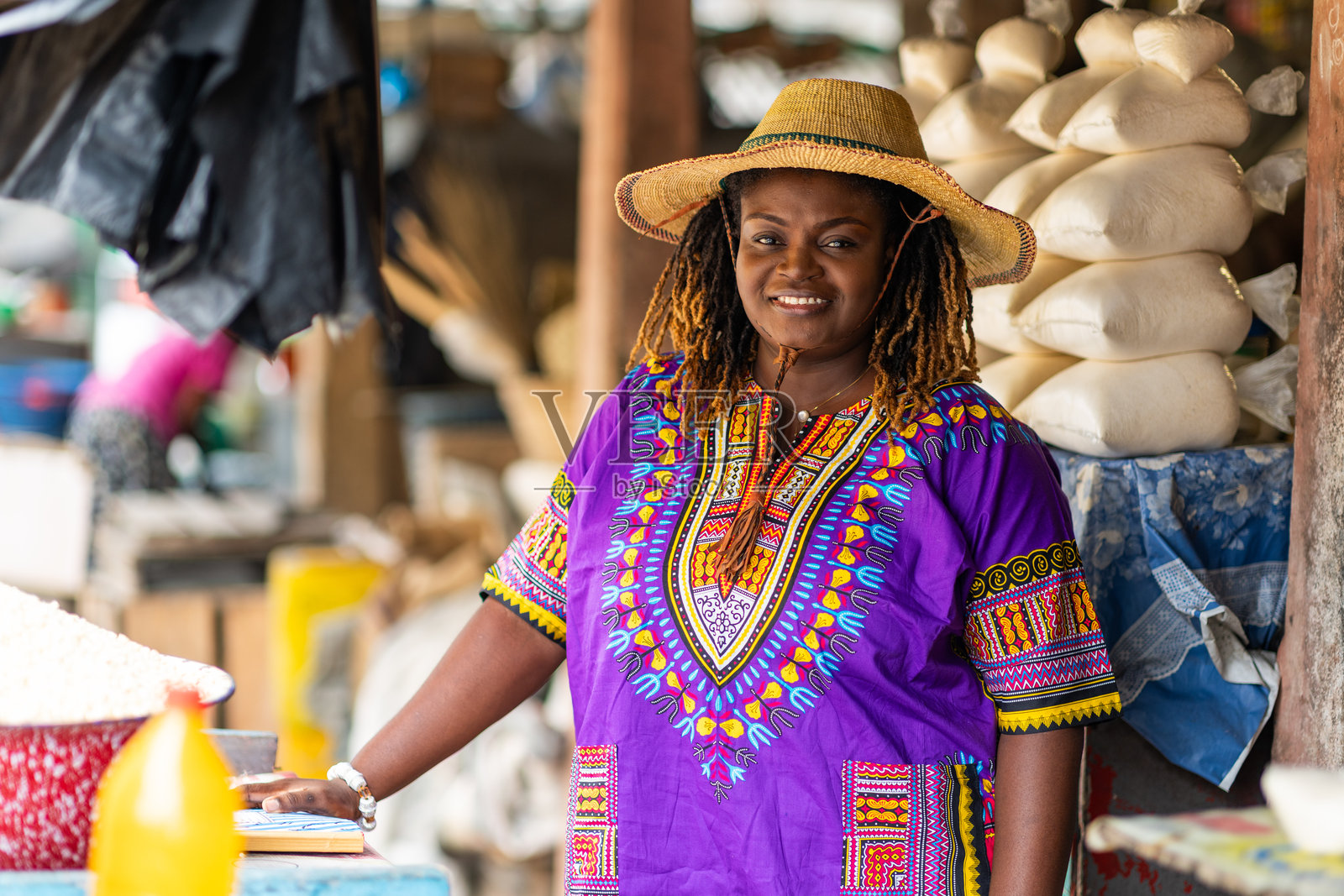 微笑的当地非洲市场女性，穿着紫色达西基和草帽。小企业主，中小企业。照片摄影图片
