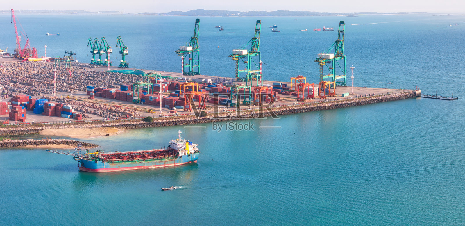 繁忙的集装箱港口，货船停靠在码头，岸边有大型起重机和堆叠的集装箱。照片摄影图片