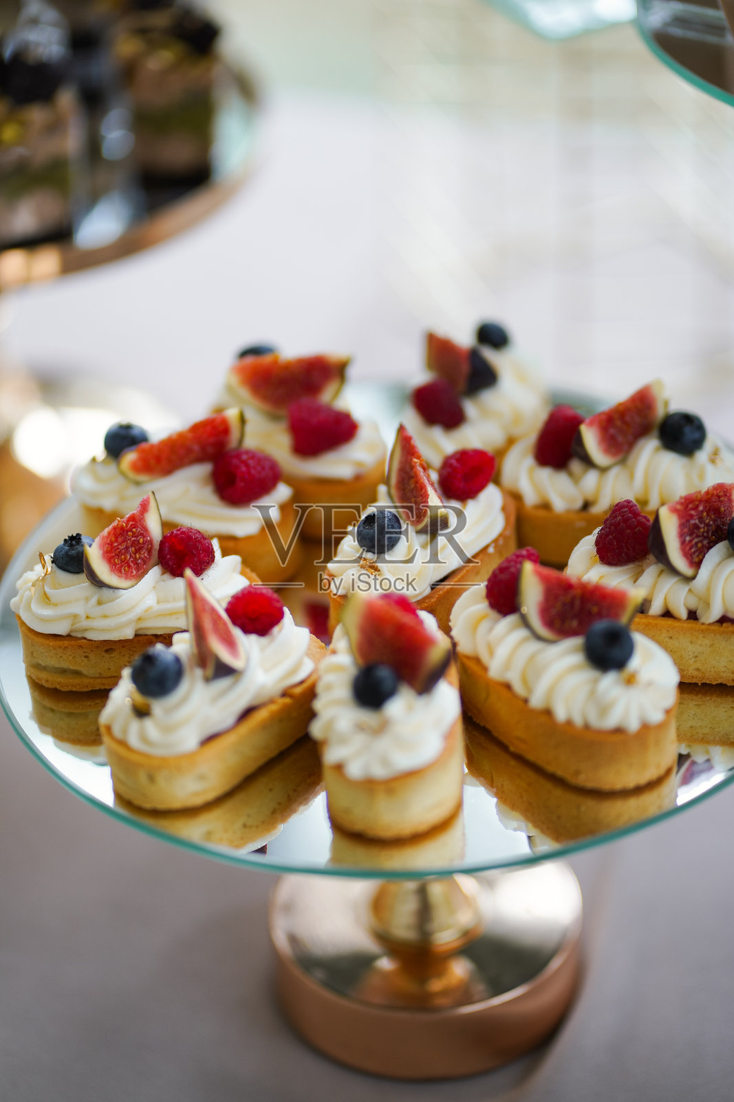 迷你蛋糕上装饰着奶油、新鲜无花果、覆盆子和蓝莓，放在镜面托盘上。照片摄影图片