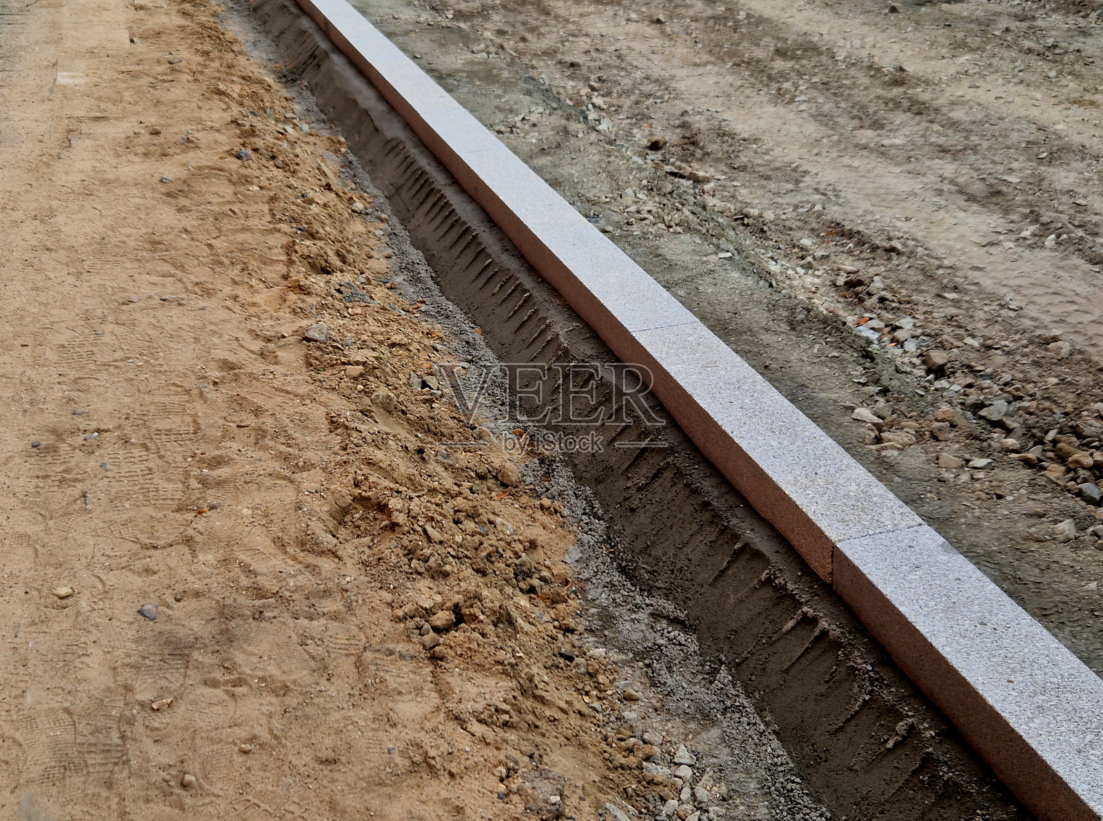 在道路上安装混凝土路缘石，当前只有混凝土基础，待铺设沥青层并进行压实。照片摄影图片