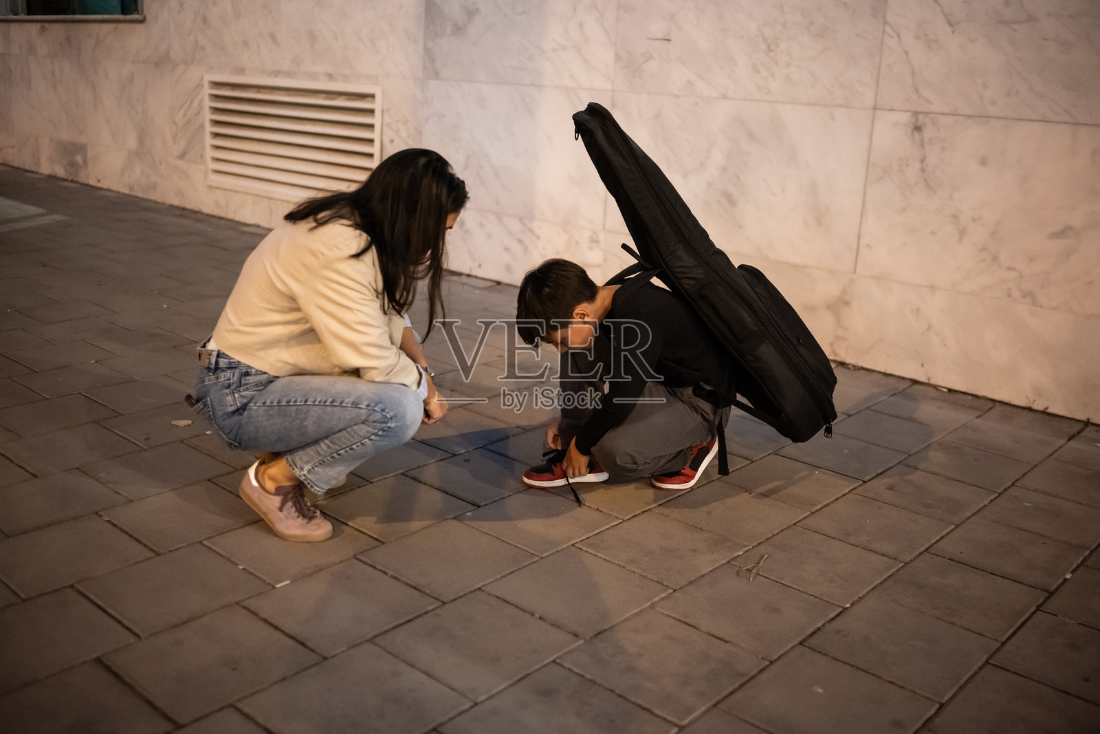 母亲在夜晚的街道上帮助儿子系鞋带照片摄影图片