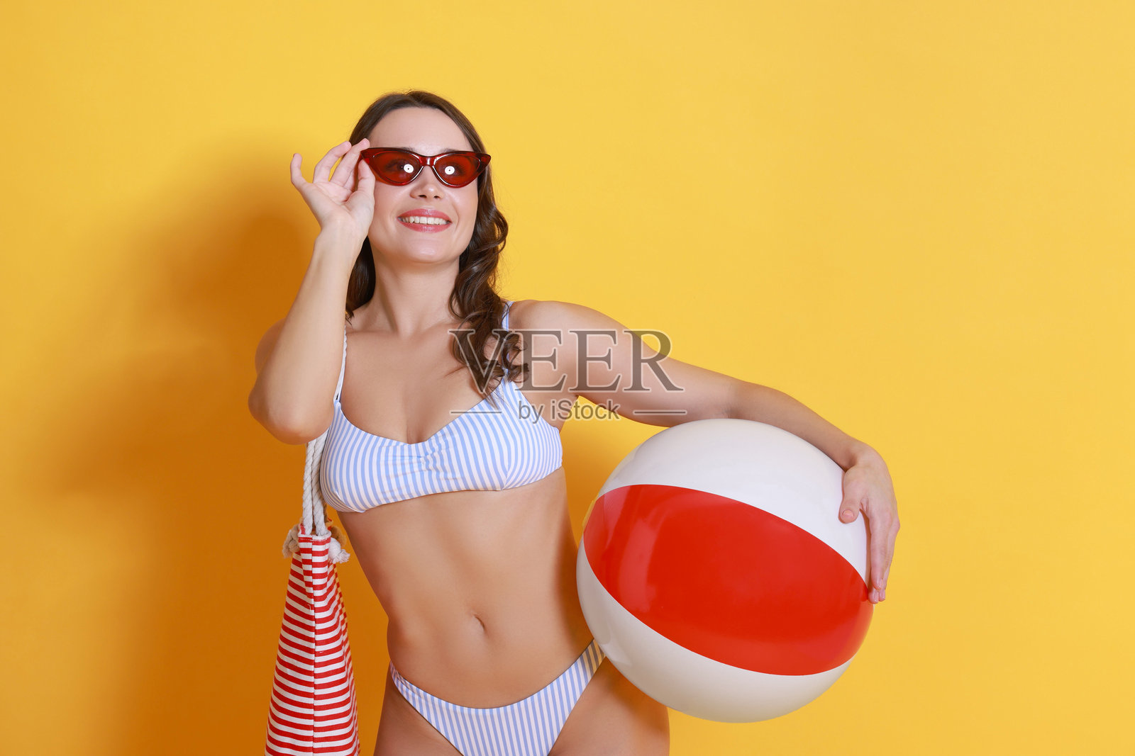 穿泳衣的美丽女性与充气球在黄色背景上照片摄影图片