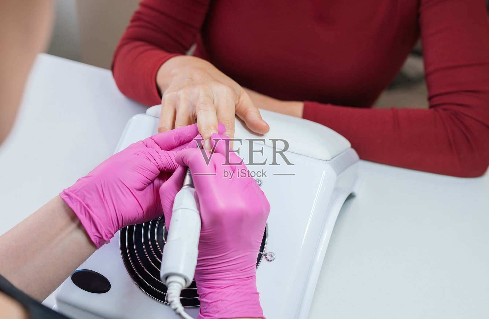 美甲专家使用电动指甲打磨工具精确修整指甲的特写照片，美容院自我护理日常，健康指甲护理和小型企业的日常工作概念。照片摄影图片