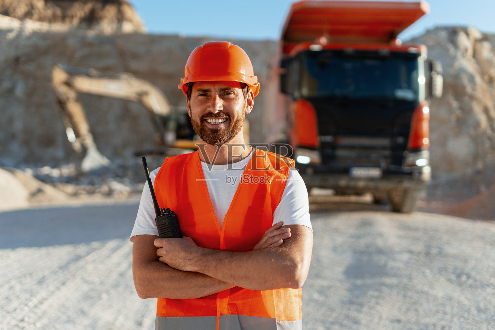 微笑的建筑工人在采石场摆姿势，双臂交叉。照片摄影图片
