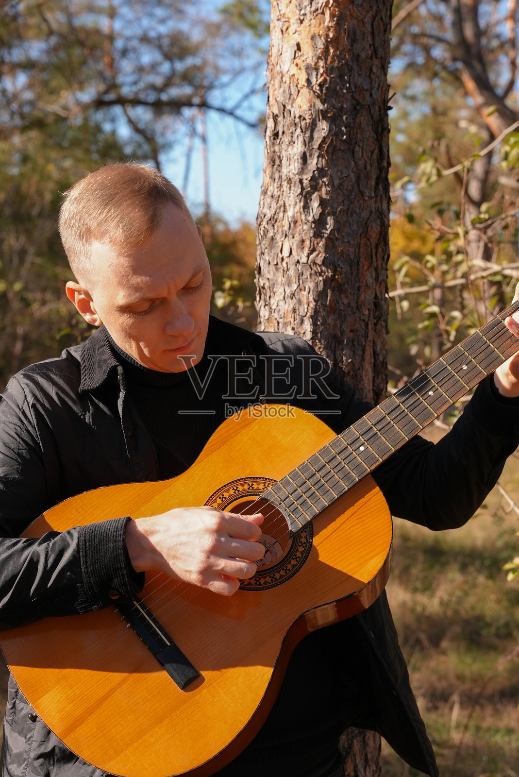 秋季森林中，一名金发男子在户外弹奏弦乐吉他。象征声音疗法、心理健康和养生仪式。宁静平和的听觉感官练习。光环能量种植。照片摄影图片