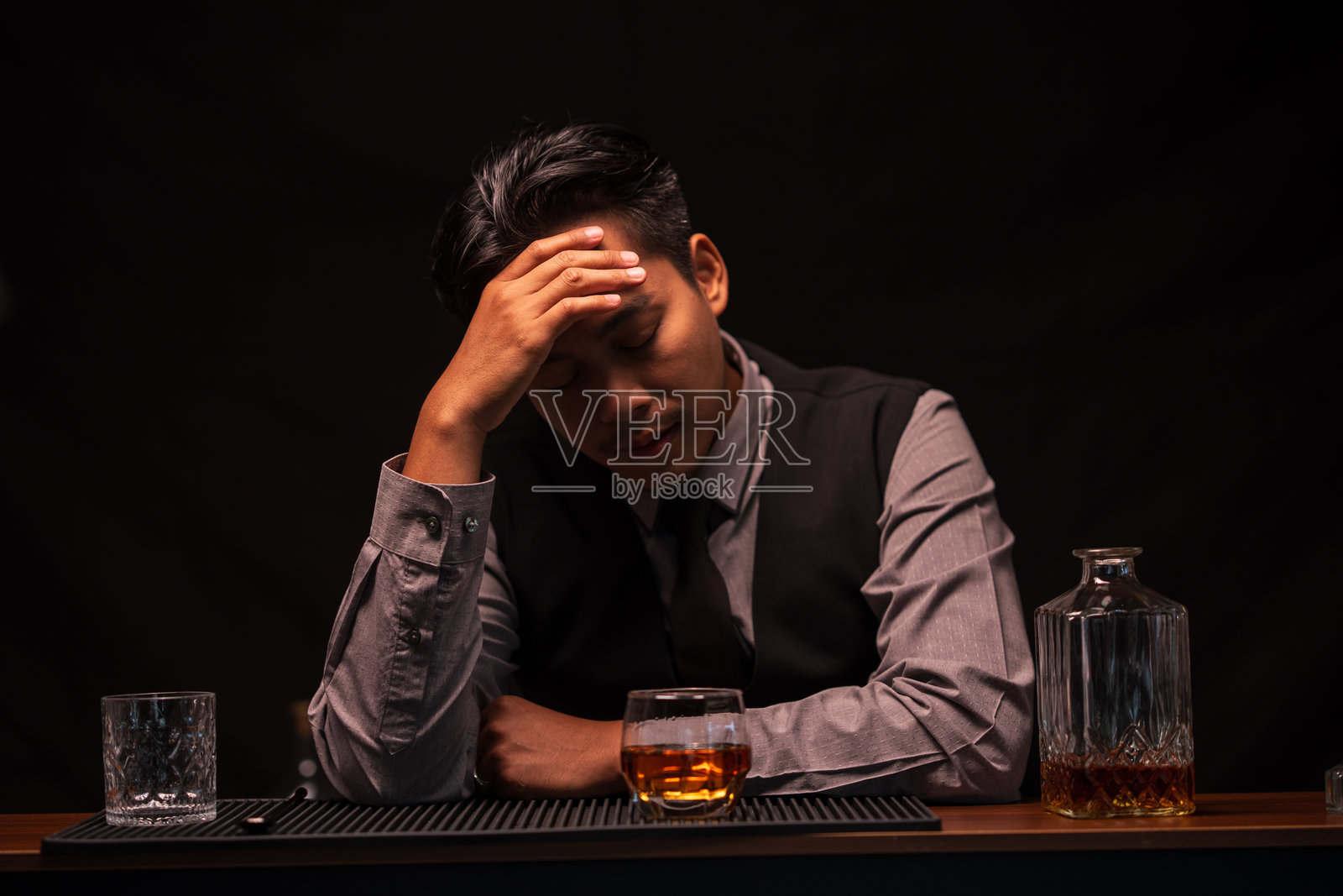 商务男士调酒师在餐厅里，忧伤地坐着，往杯子里倒威士忌。照片摄影图片