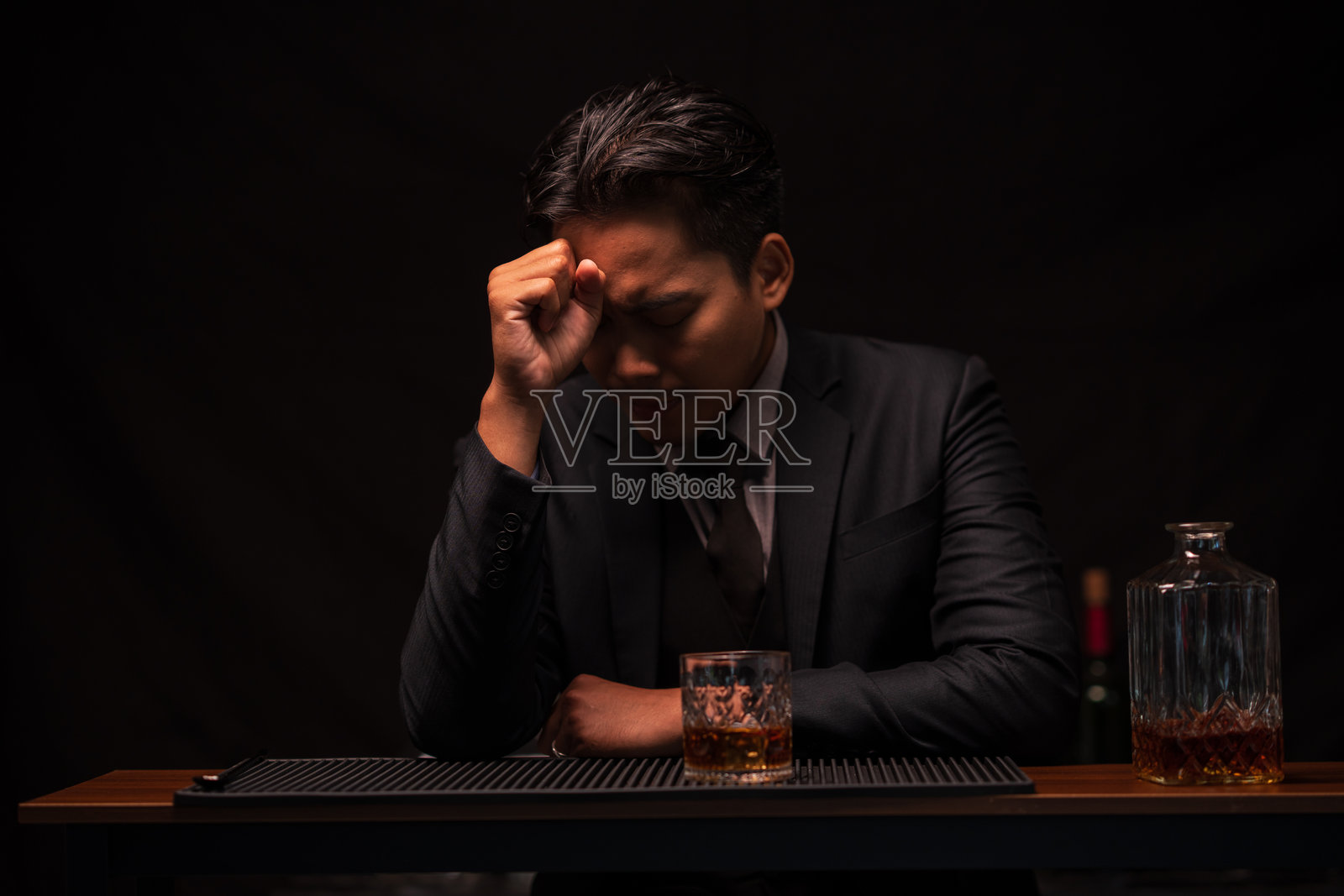 身穿西装的酒保在餐厅里，悲伤地坐在那里，一边往杯子里倒威士忌。照片摄影图片