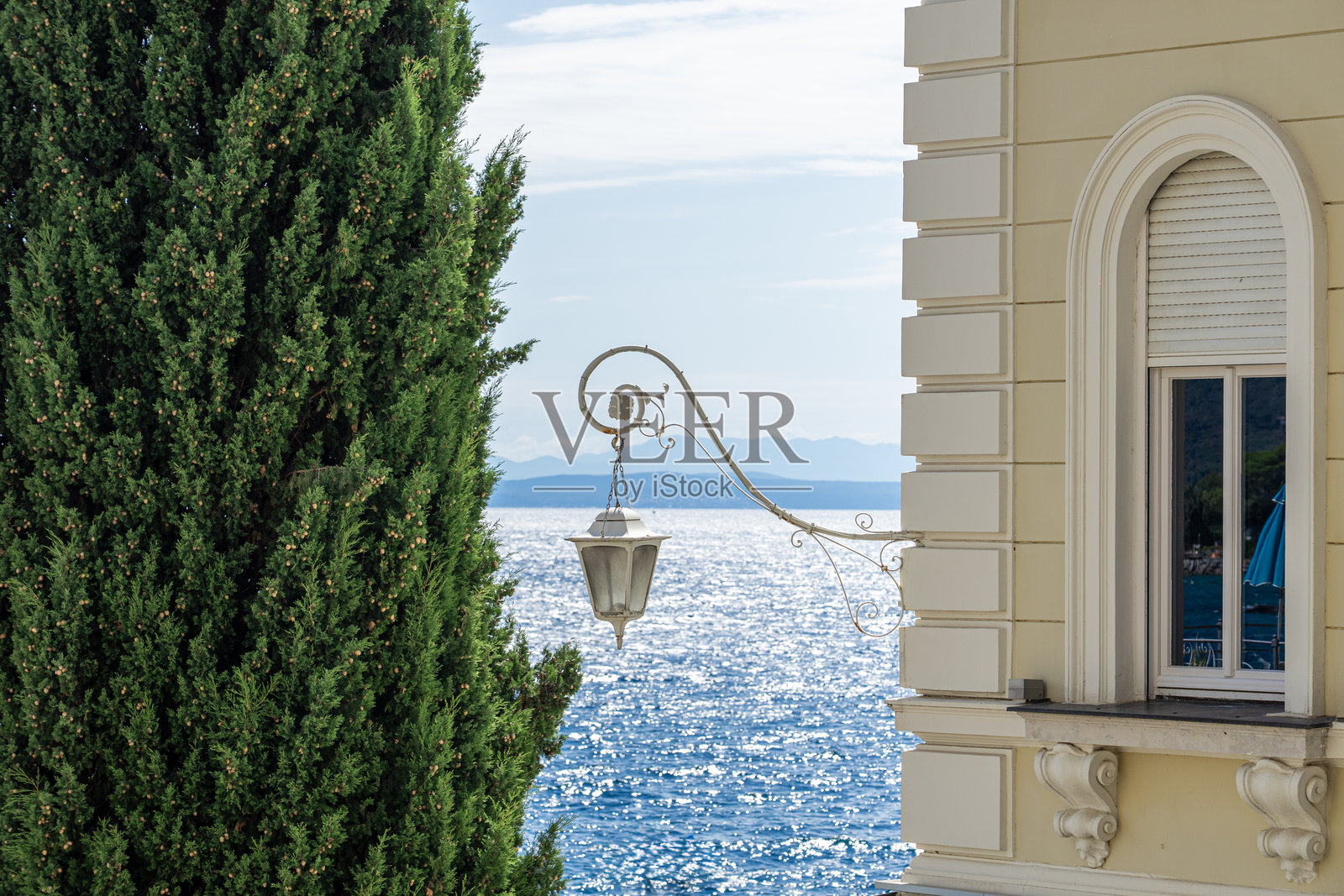 克罗地亚奥帕蒂亚，海边优雅的风景，配有古典灯、丝柏树和闪耀的蓝色大海。照片摄影图片