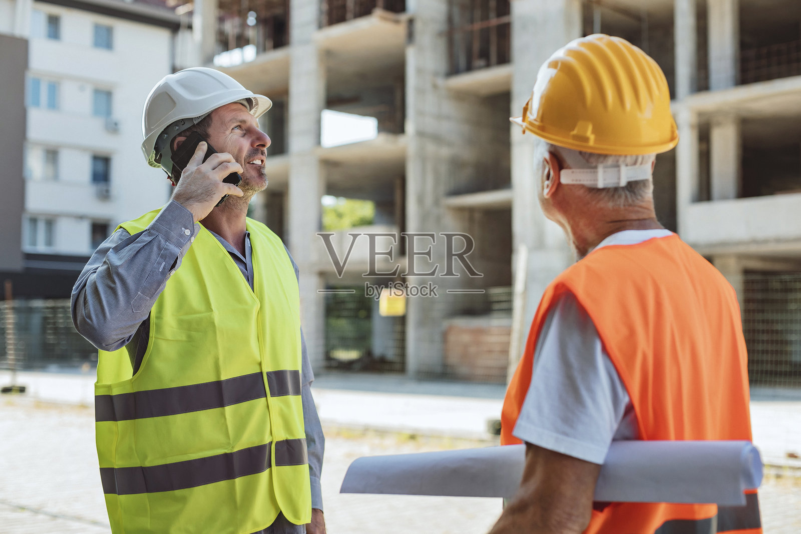 经理在电话中协调任务，工人拿着蓝图站在旁边照片摄影图片