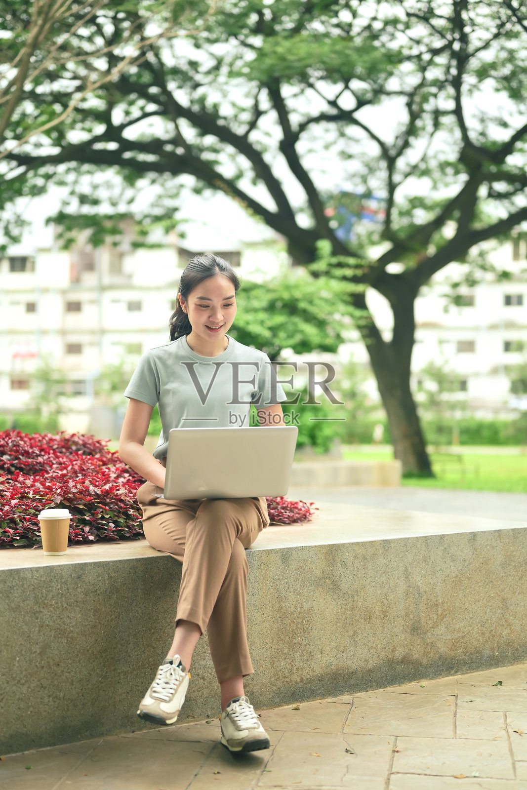 休闲风的年轻女子坐在户外的植物旁，正在用笔记本电脑打字照片摄影图片