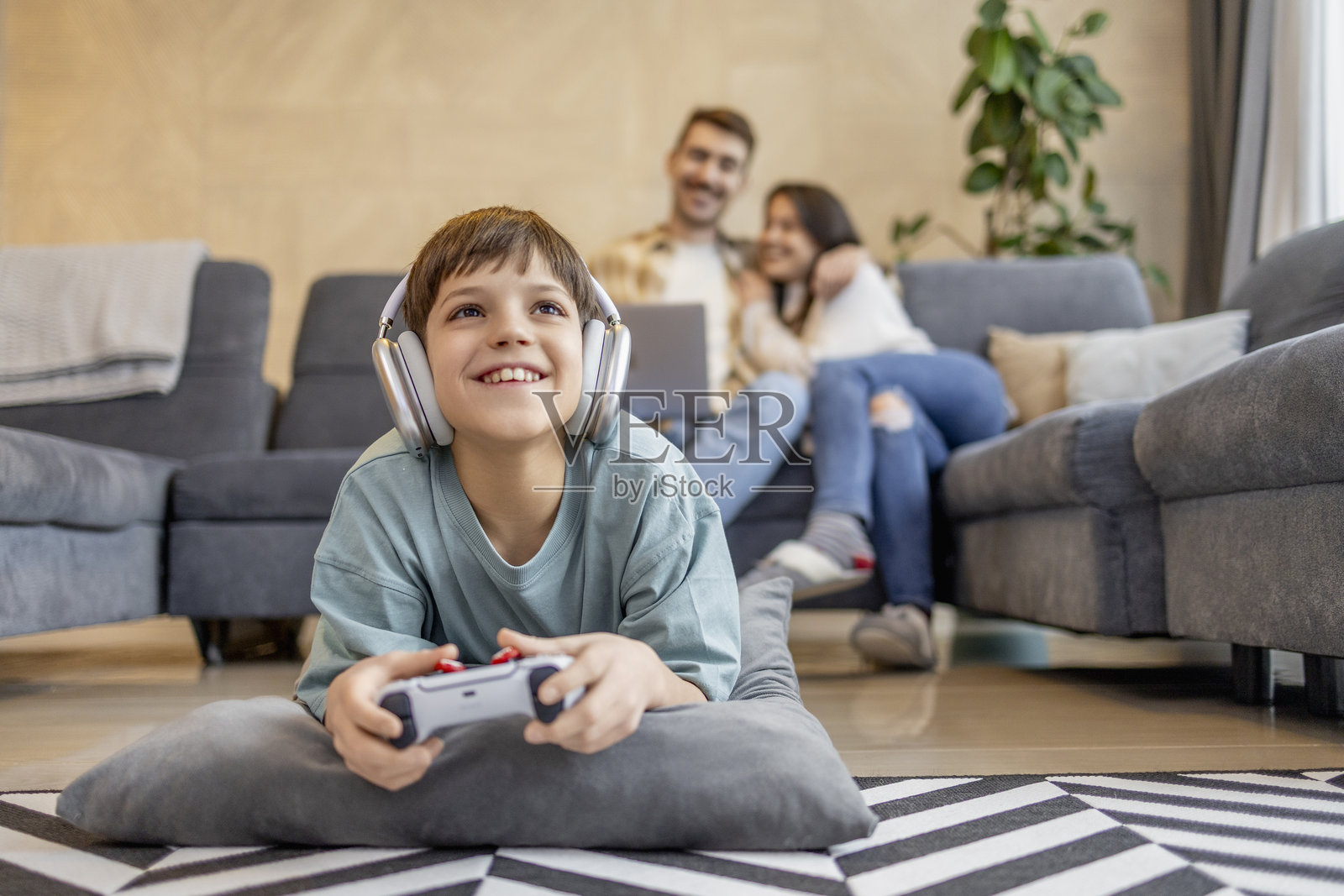 小男孩在家玩电子游戏，家人在背景中享受时光照片摄影图片