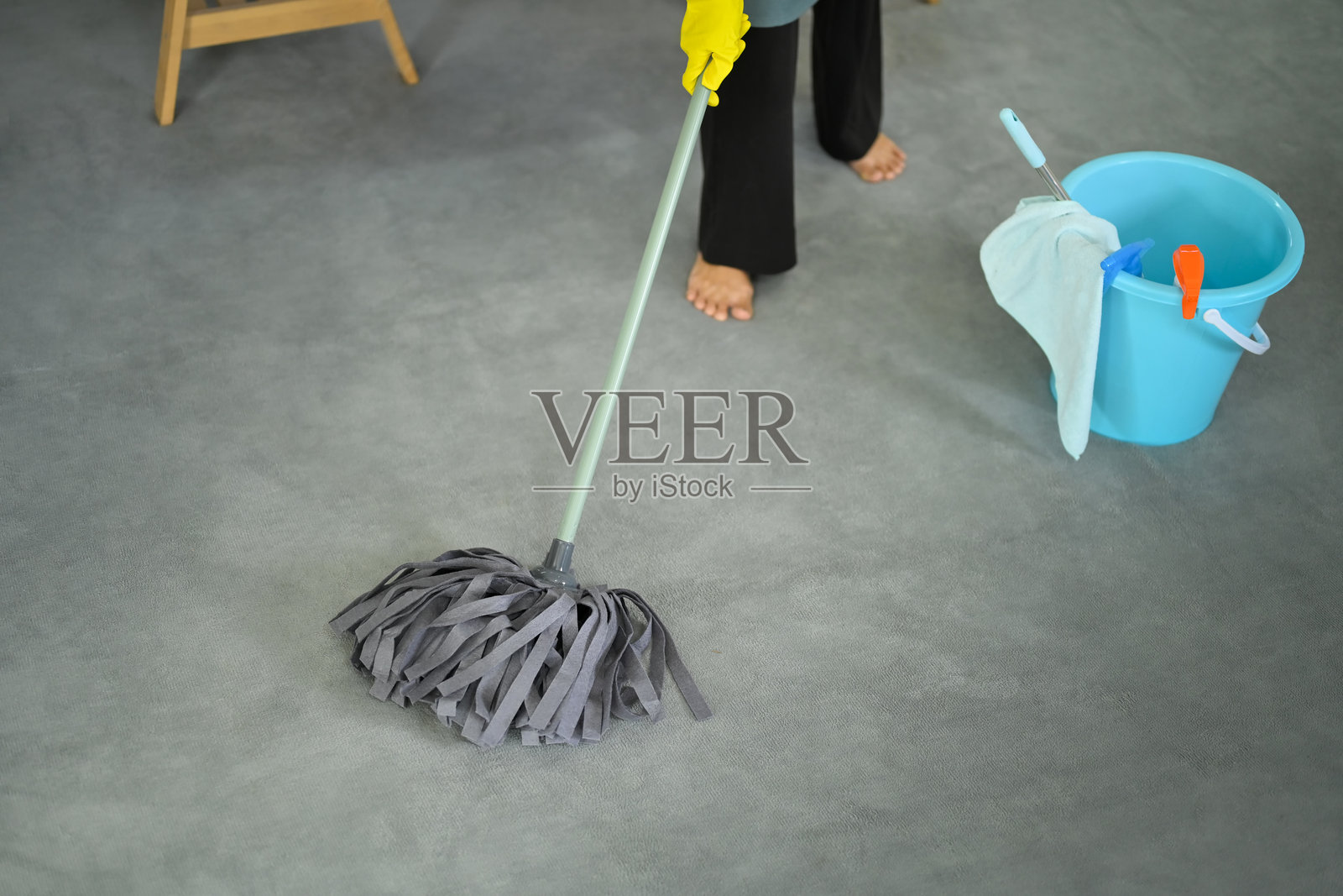 身穿黄色手套的人用蓝色水桶和清洁工具拖地，地板是灰色的。照片摄影图片