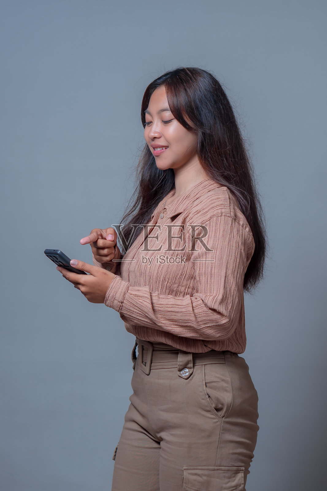 一位年轻的亚洲印度尼西亚女性侧面视图，她微笑着使用智能手机。描绘了现代数字生活方式、技术使用和日常生活中的移动通信。照片摄影图片