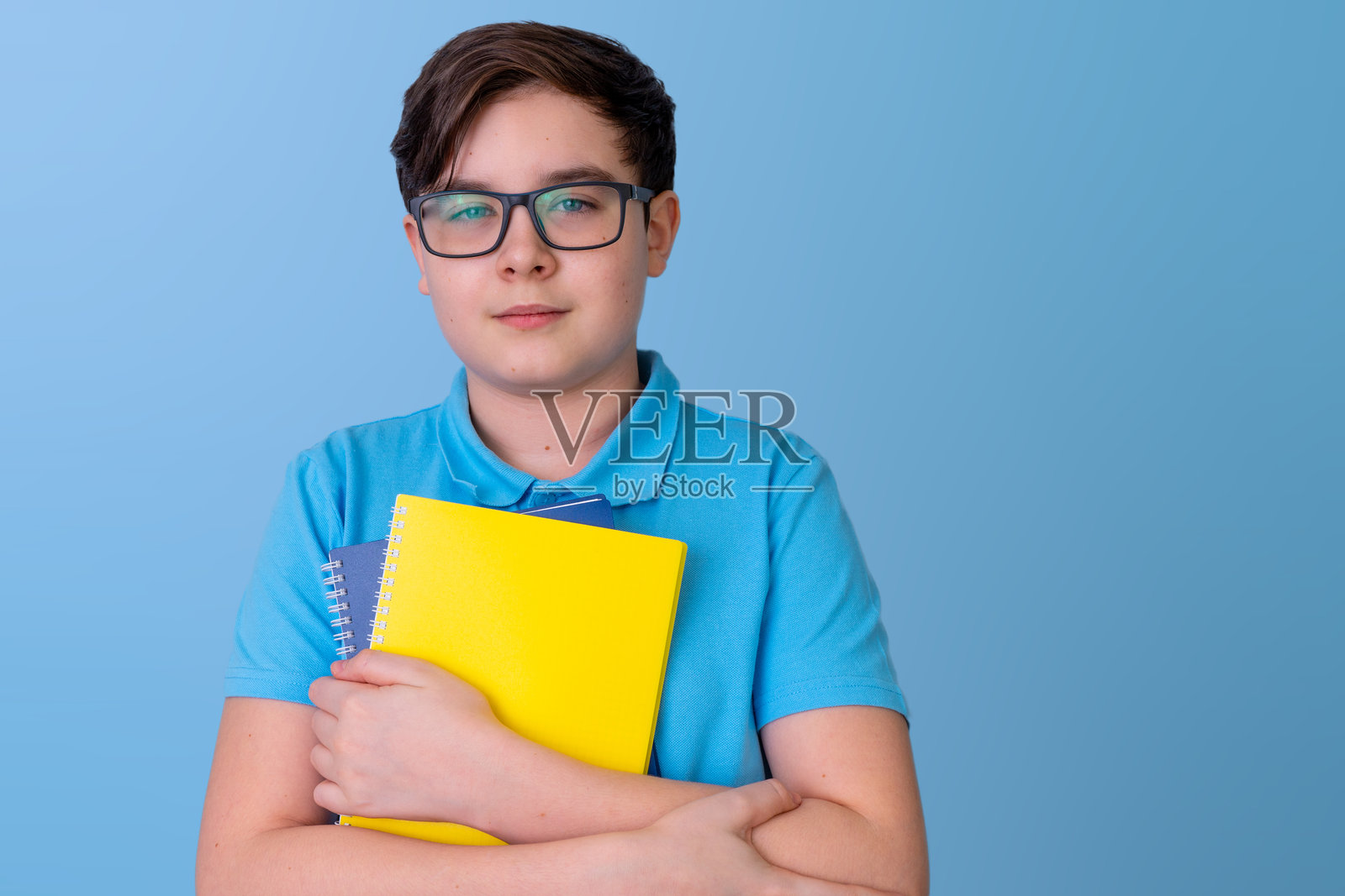 自信的白人男性青少年，手持笔记本，背景为蓝色，表情自信。照片摄影图片