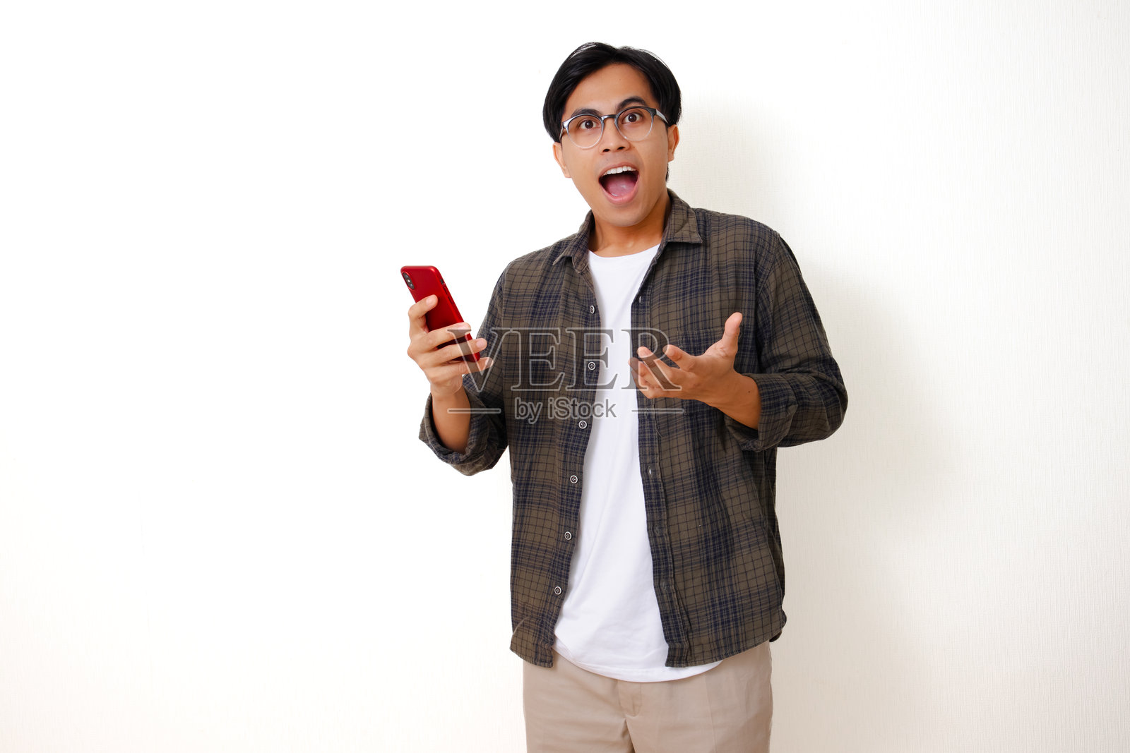 惊喜的年轻亚洲男子看着手机，脸上露出惊叹的表情，孤立在白色背景上。照片摄影图片