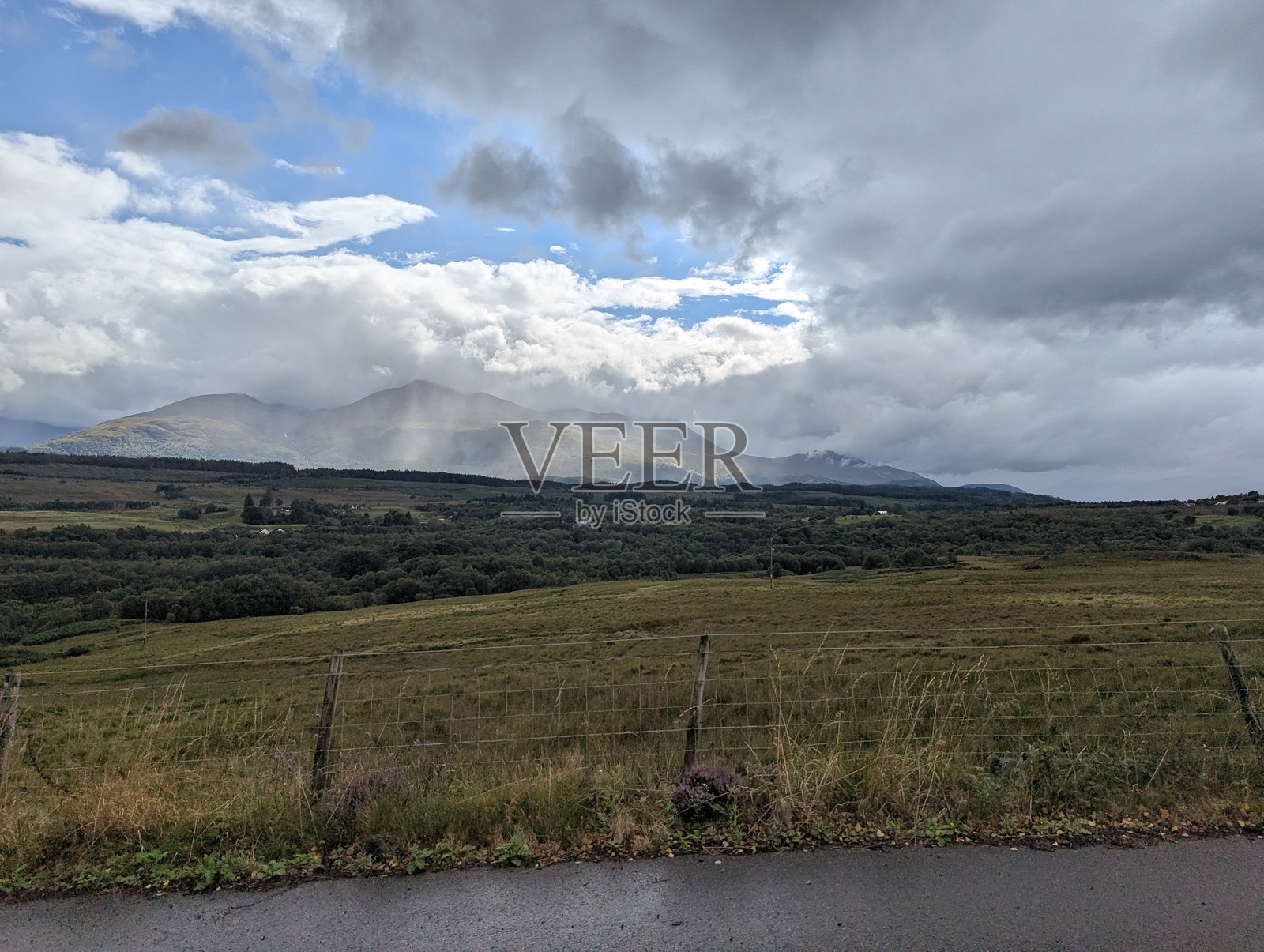 雾气弥漫的山脉、起伏的绿色田野和暴风雨般的天空，苏格兰高地戏剧性的景观。照片摄影图片