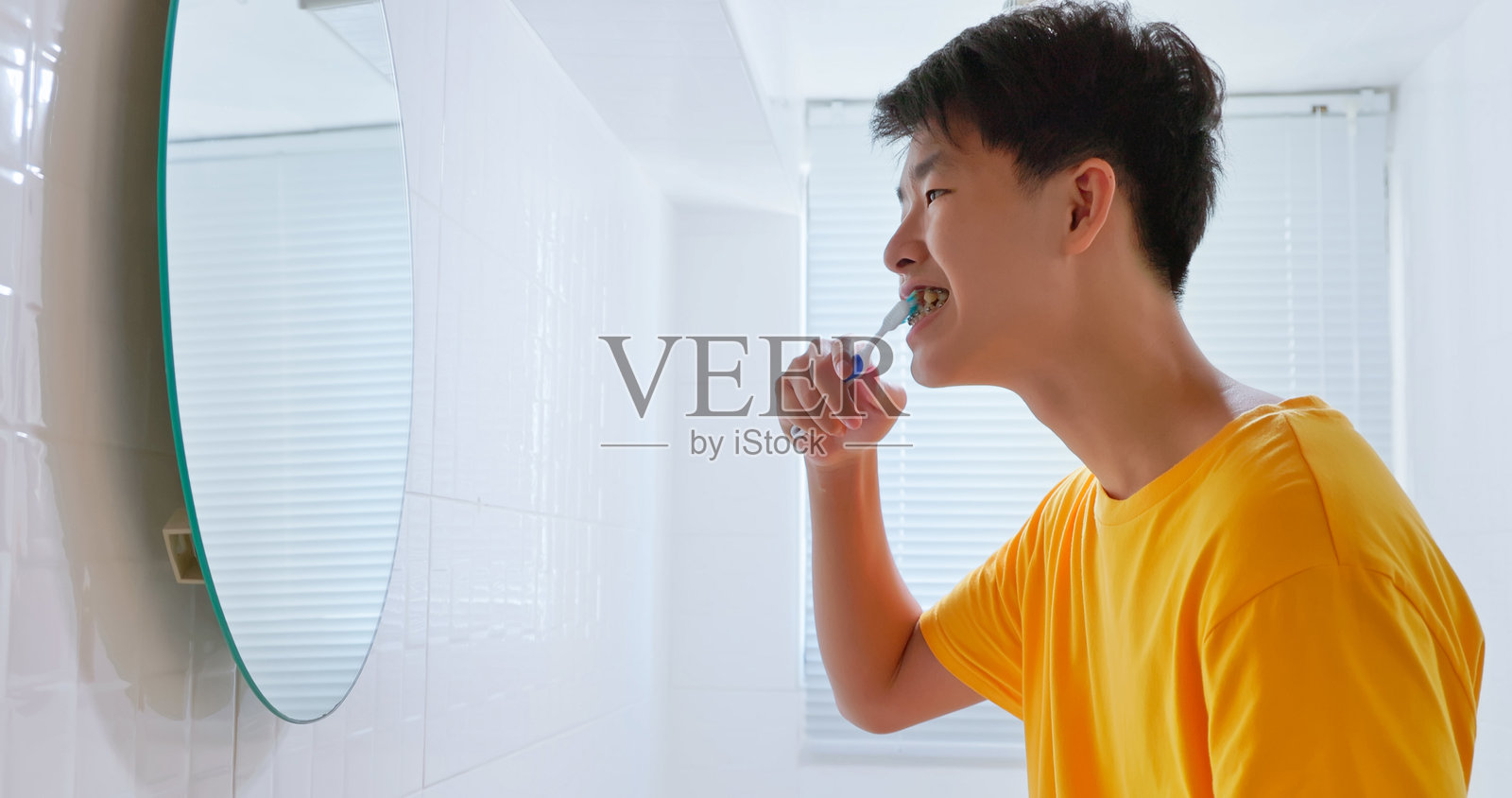 青少年在浴室里对着镜子刷牙套。照片摄影图片