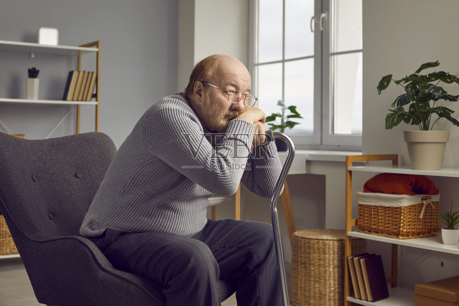 悲伤孤独的老年男子坐在扶手椅上，旁边放着拐杖照片摄影图片